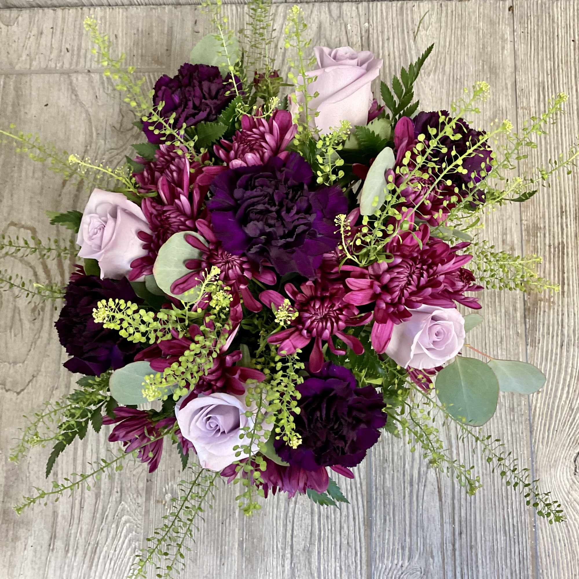 Round bouquet of purple and lavender flowers with airy greenery