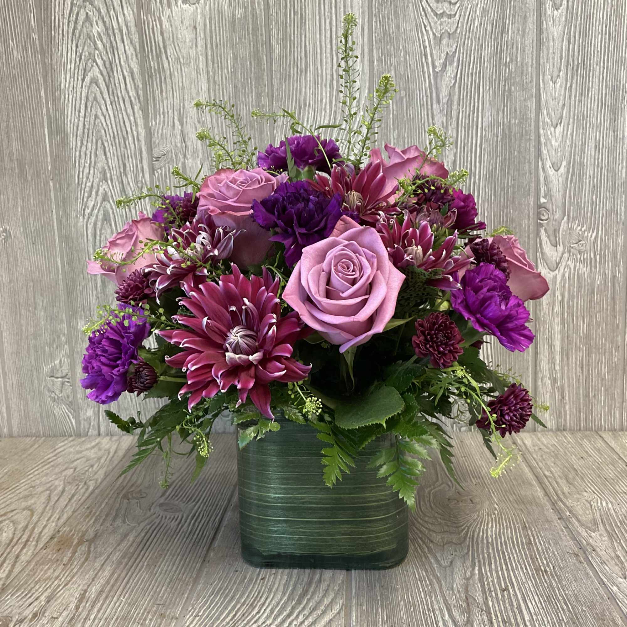 Pink and purple flower arrangement in a green square vase
