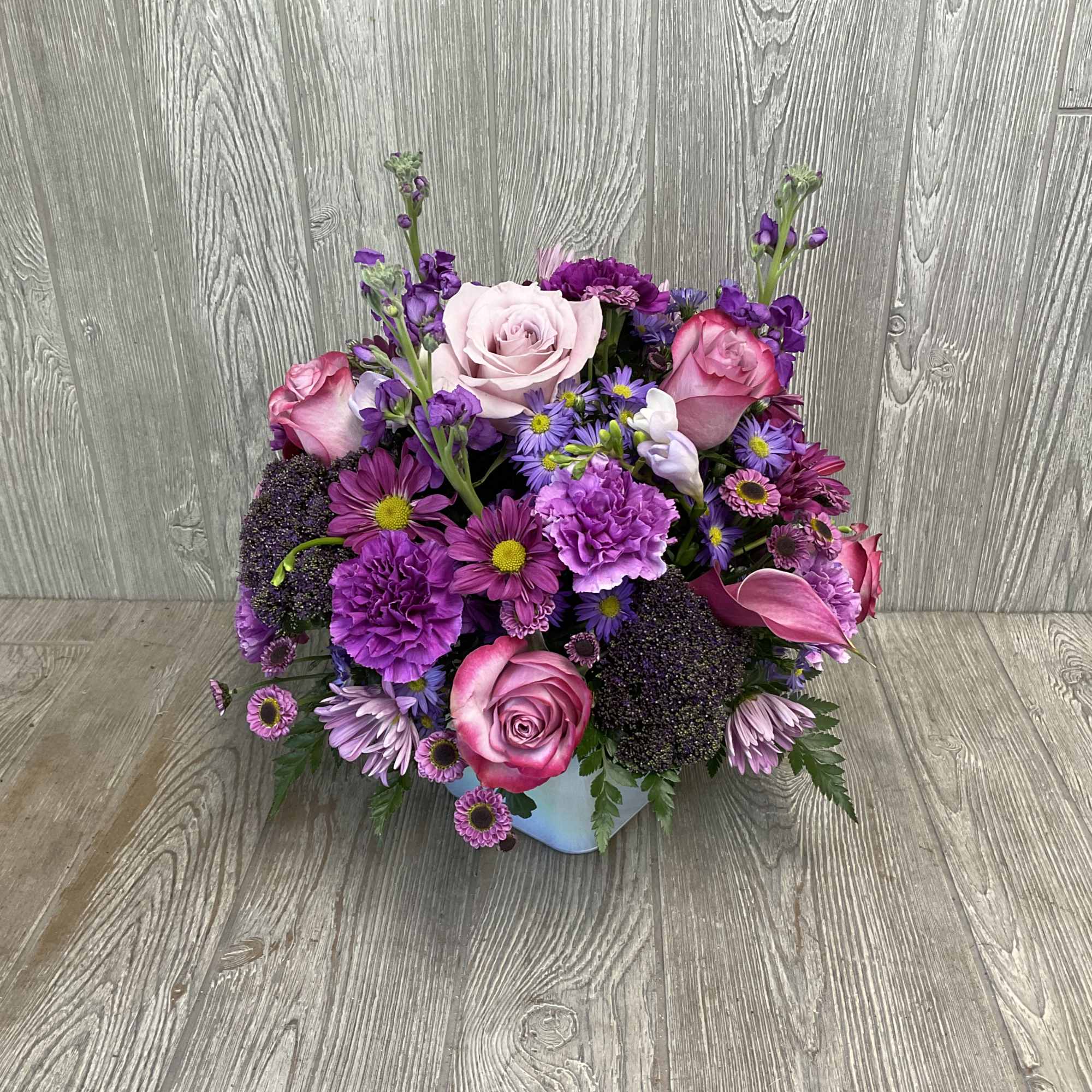 Pink and purple mixed flower arrangement in a light blue container