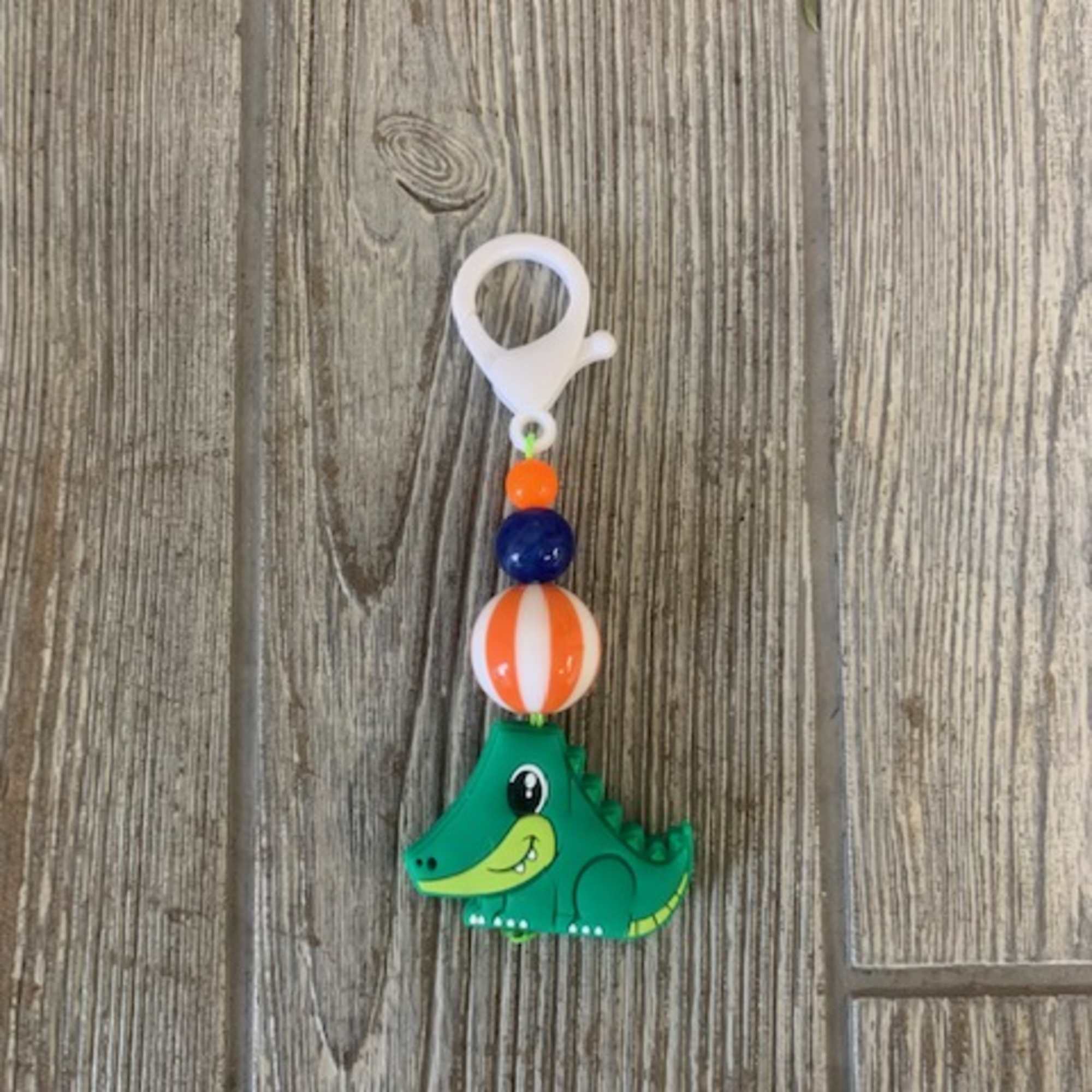Green dinosaur keychain with colorful beads on a white clip