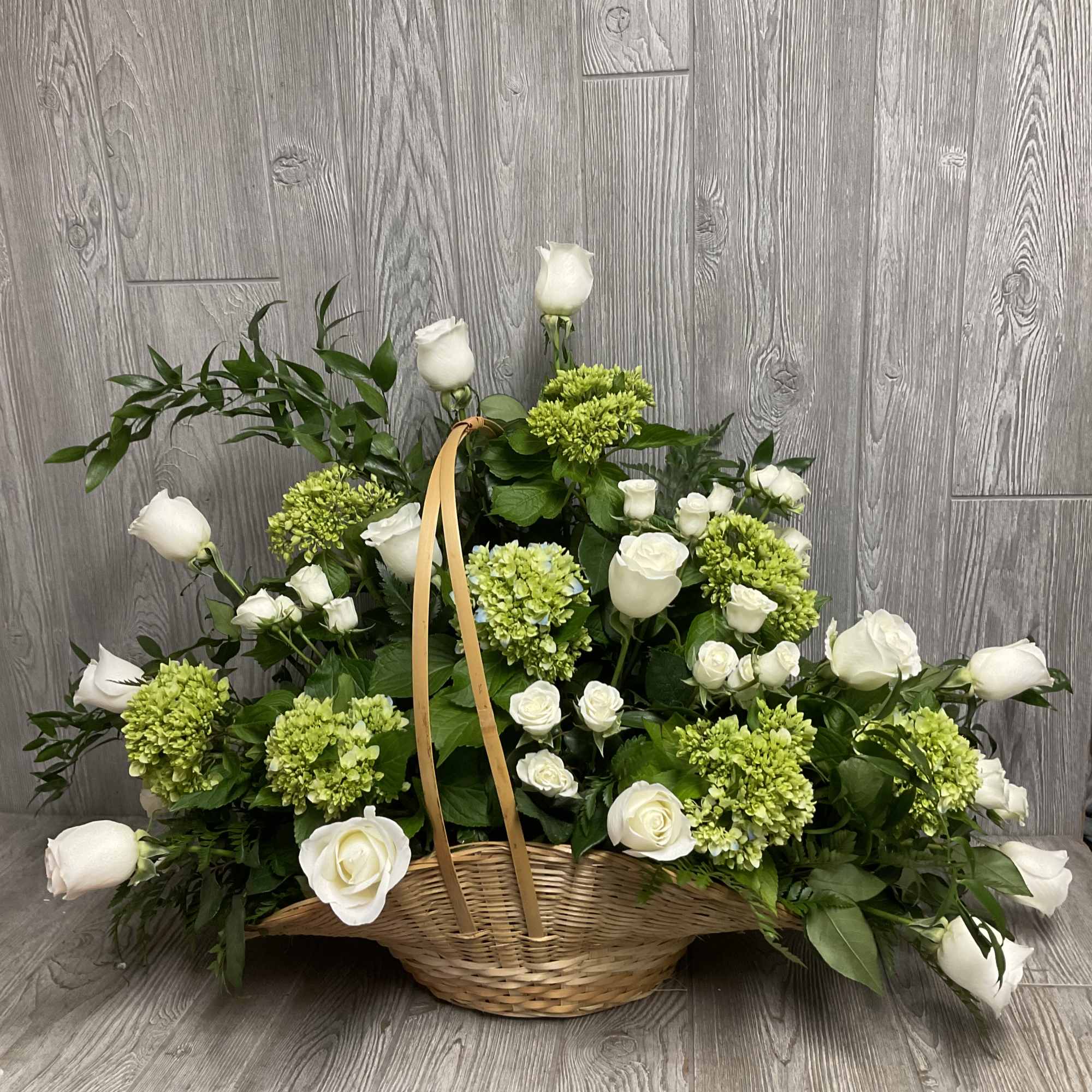 Basket arrangement of white roses and green hydrangeas