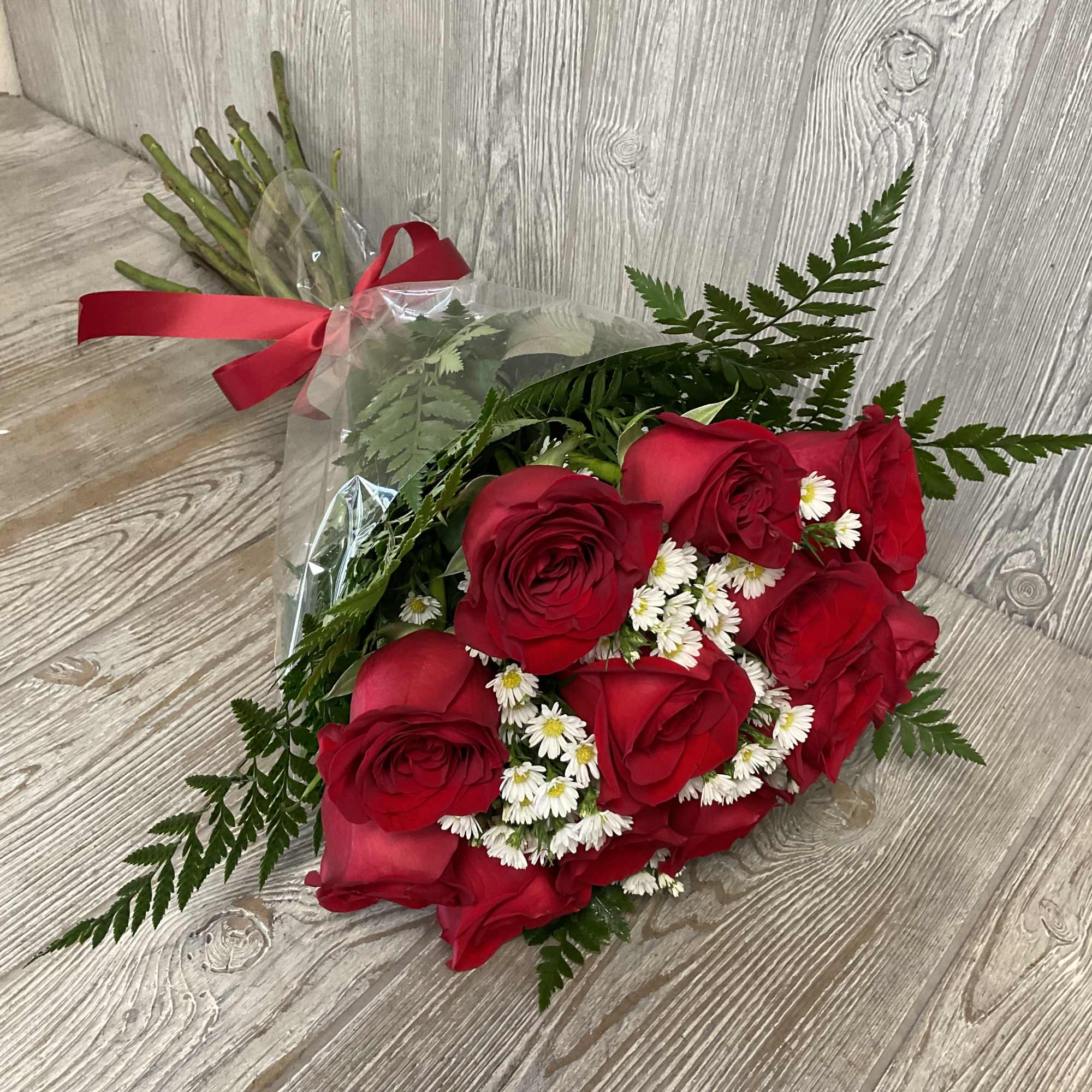 Hand-tied bouquet of red roses with small white daisies wrapped in clear cellophane and tied with a red ribbon.
