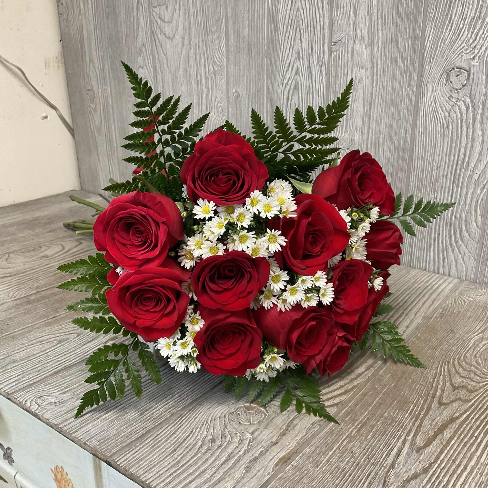 Hand-tied bouquet of red roses with small white daisy flowers