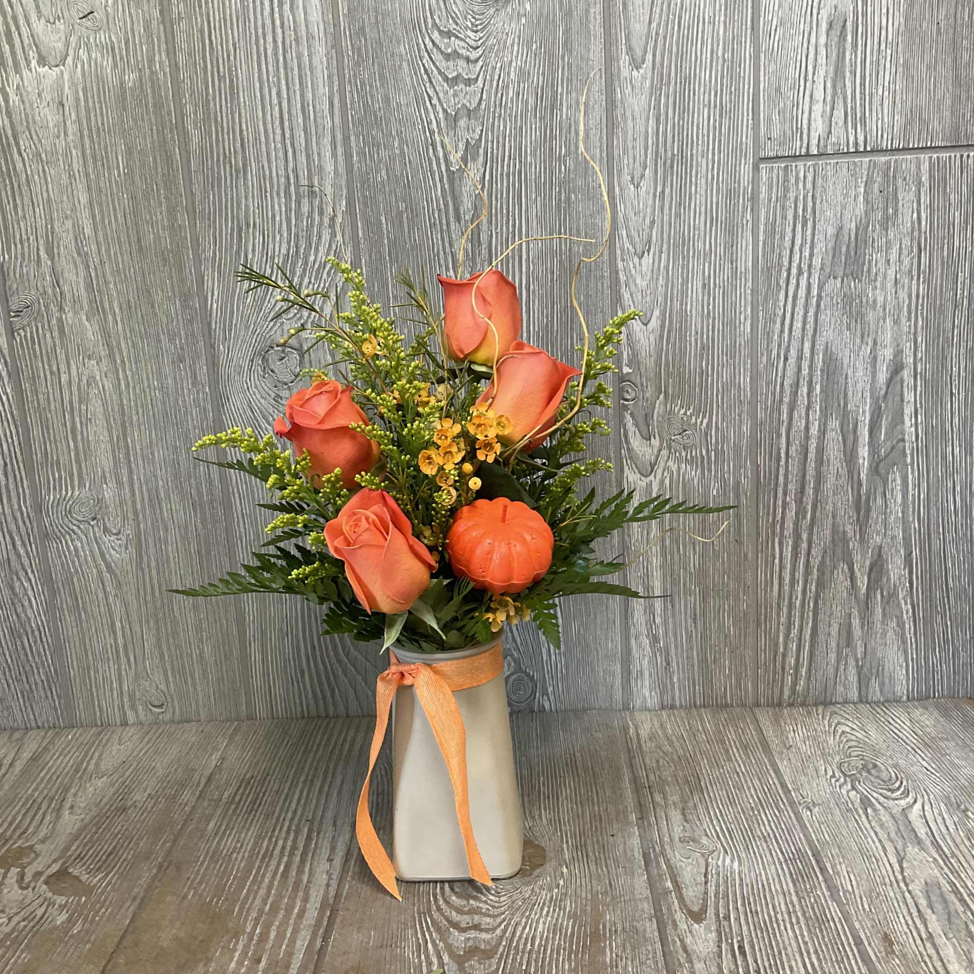 Orange roses in a tall vase with a ribbon and small pumpkin accent