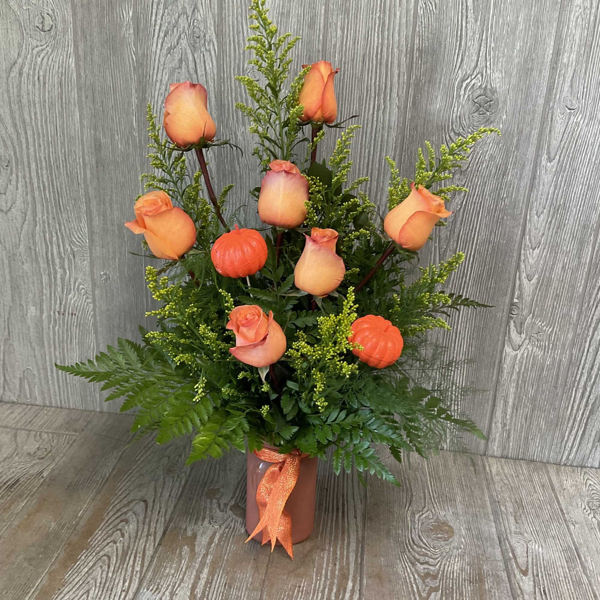 Orange roses arranged in a vase with greenery and small pumpkin accents