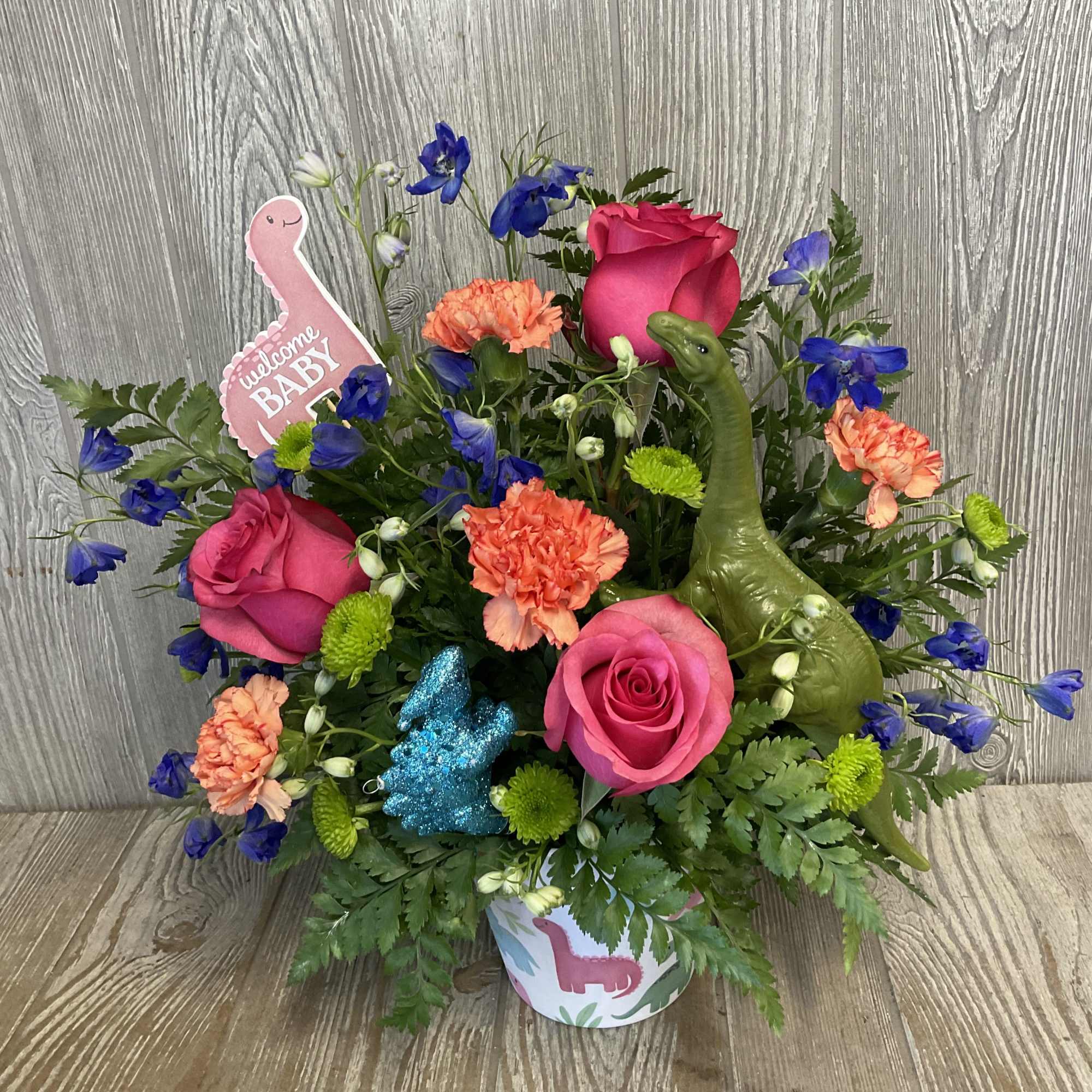 Colorful bouquet with pink roses, orange carnations, and blue flowers in a baby-themed container