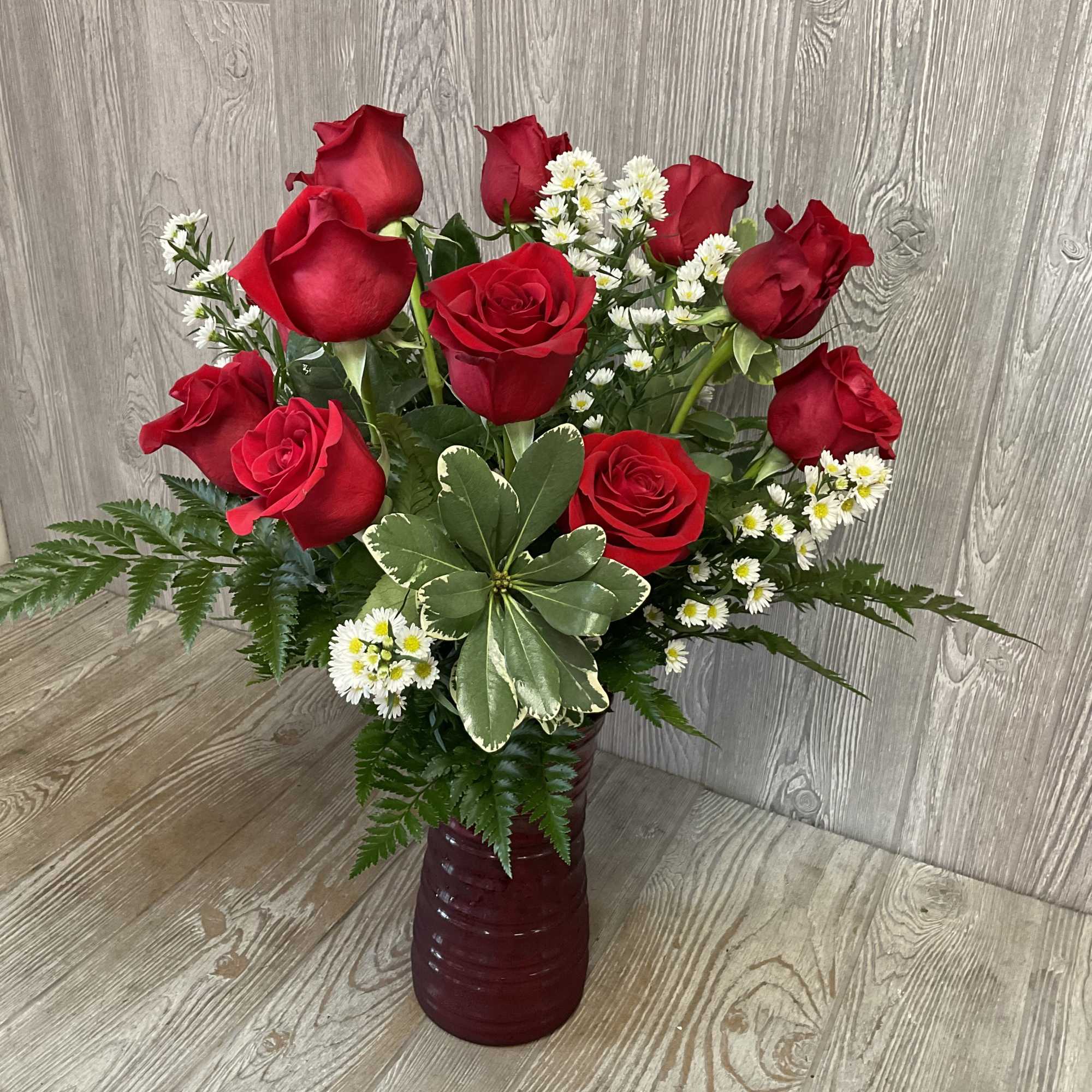 Red roses and white daisies arranged in a burgundy vase.