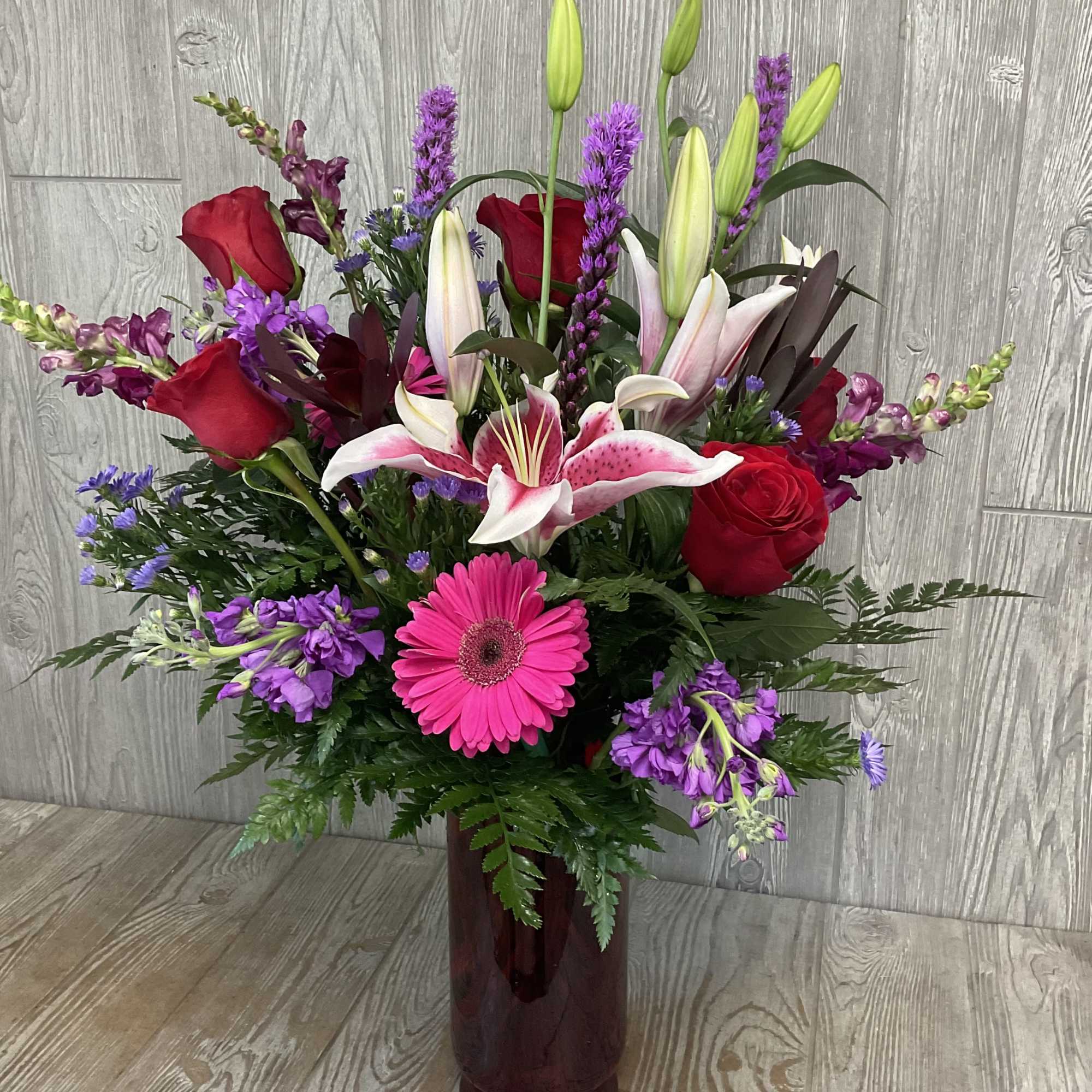 Mixed bouquet of red roses, pink lilies, and purple flowers in a tall vase