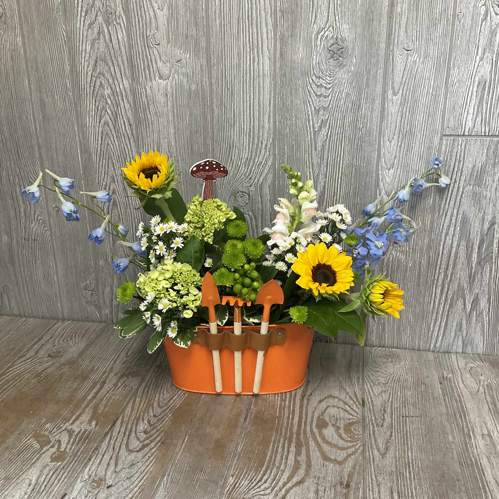 Flower arrangement in an orange container with small garden tools