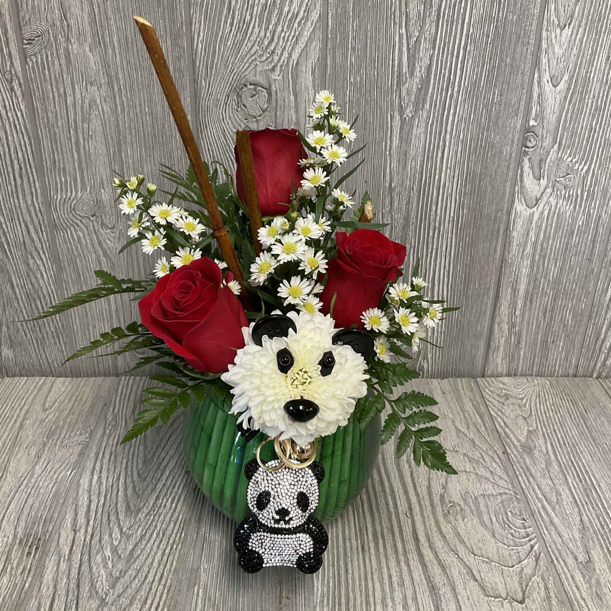 Red roses and white daisies arranged in a green vase with a panda ornament
