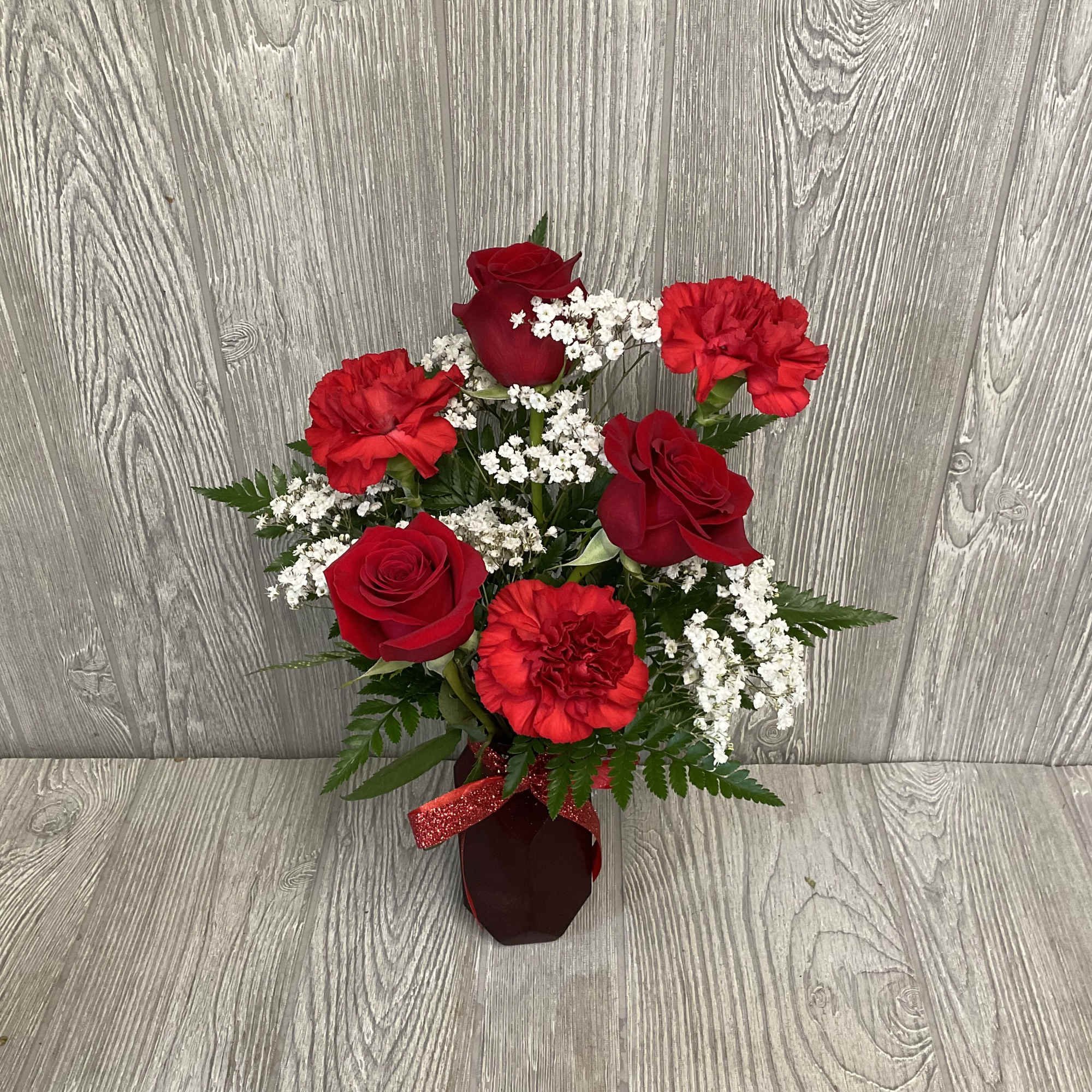Red roses and carnations in a small vase with white filler flowers
