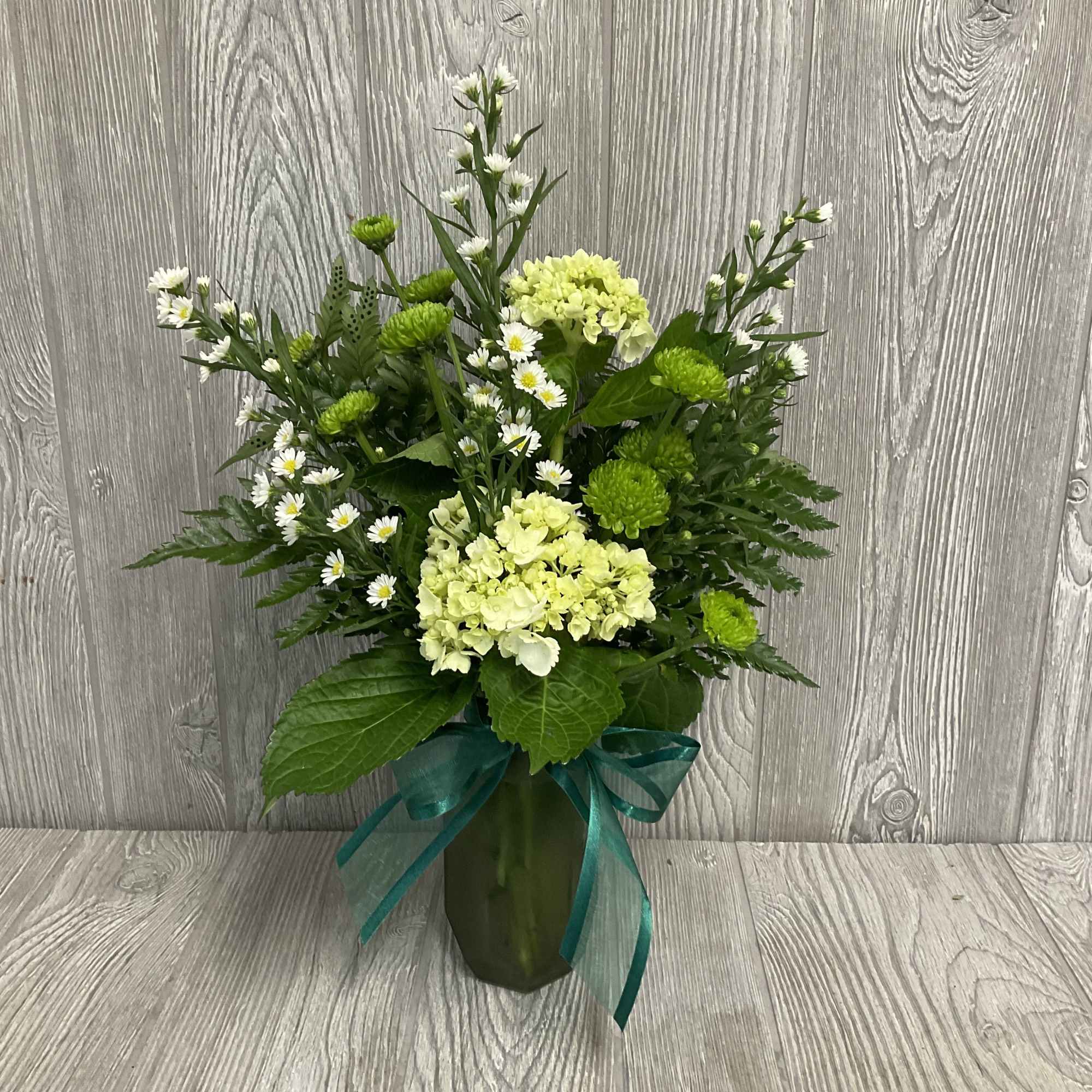 Green and white floral arrangement in a vase with a teal ribbon
