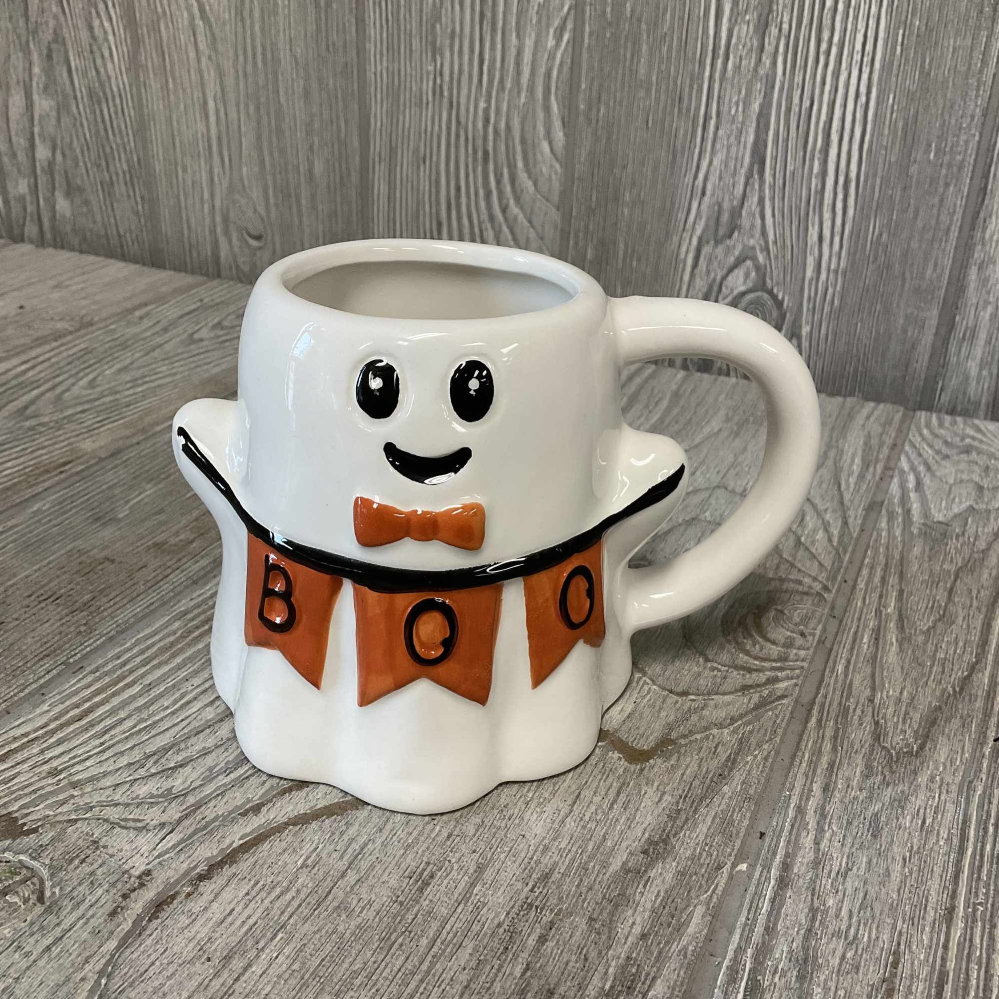 Ghost-shaped ceramic mug with a smiling face and orange bow tie