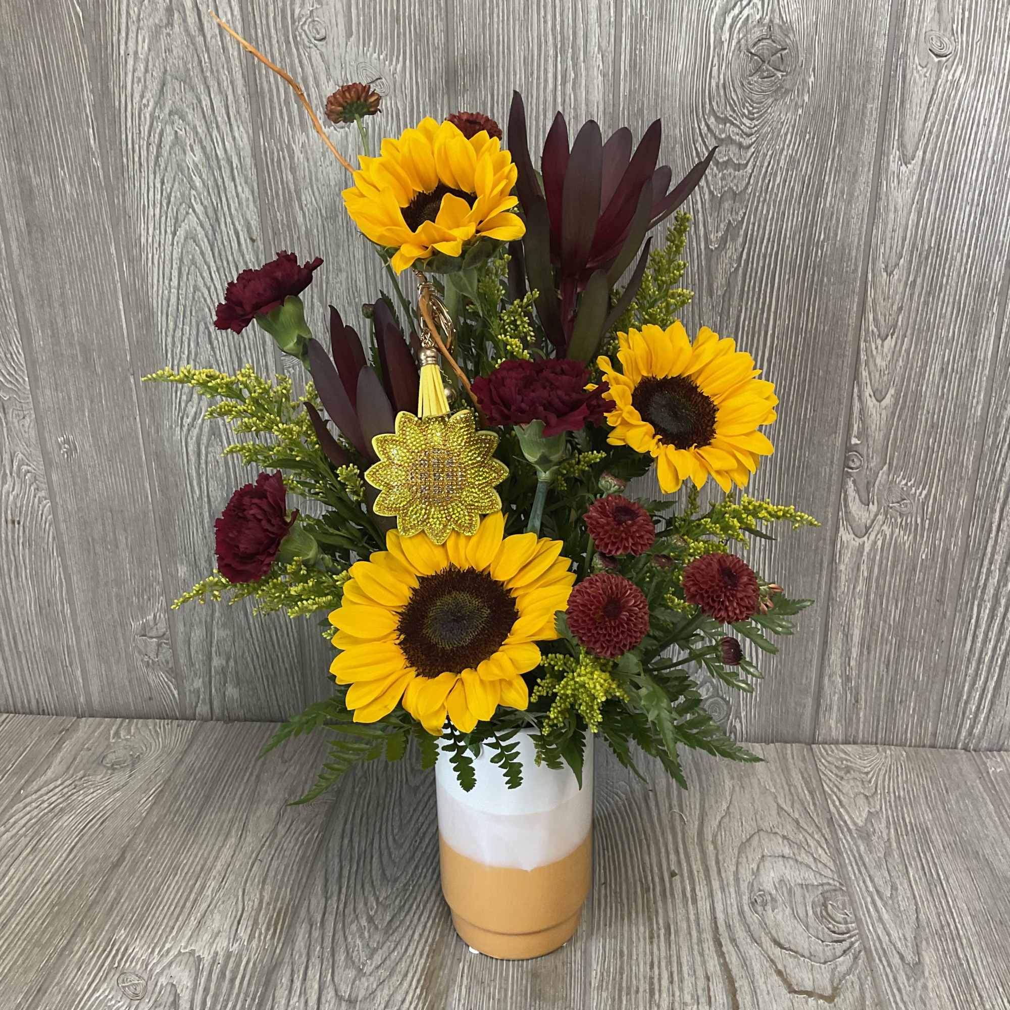 Sunflowers and burgundy carnations in a white and orange vase