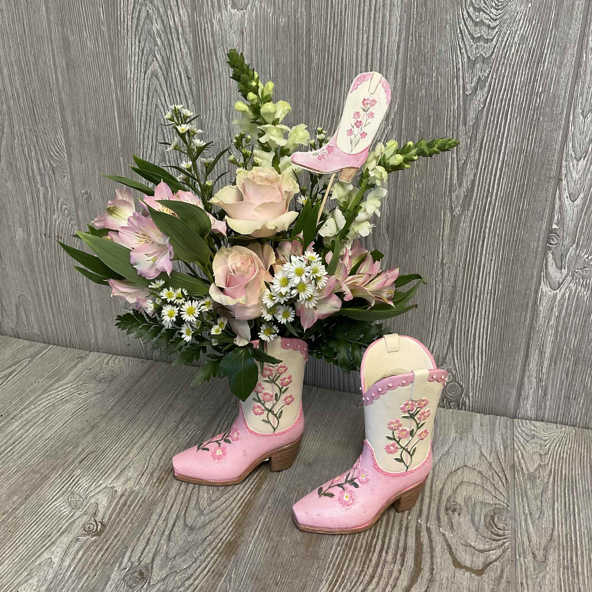 Pink cowboy boots holding a floral arrangement with roses and daisies