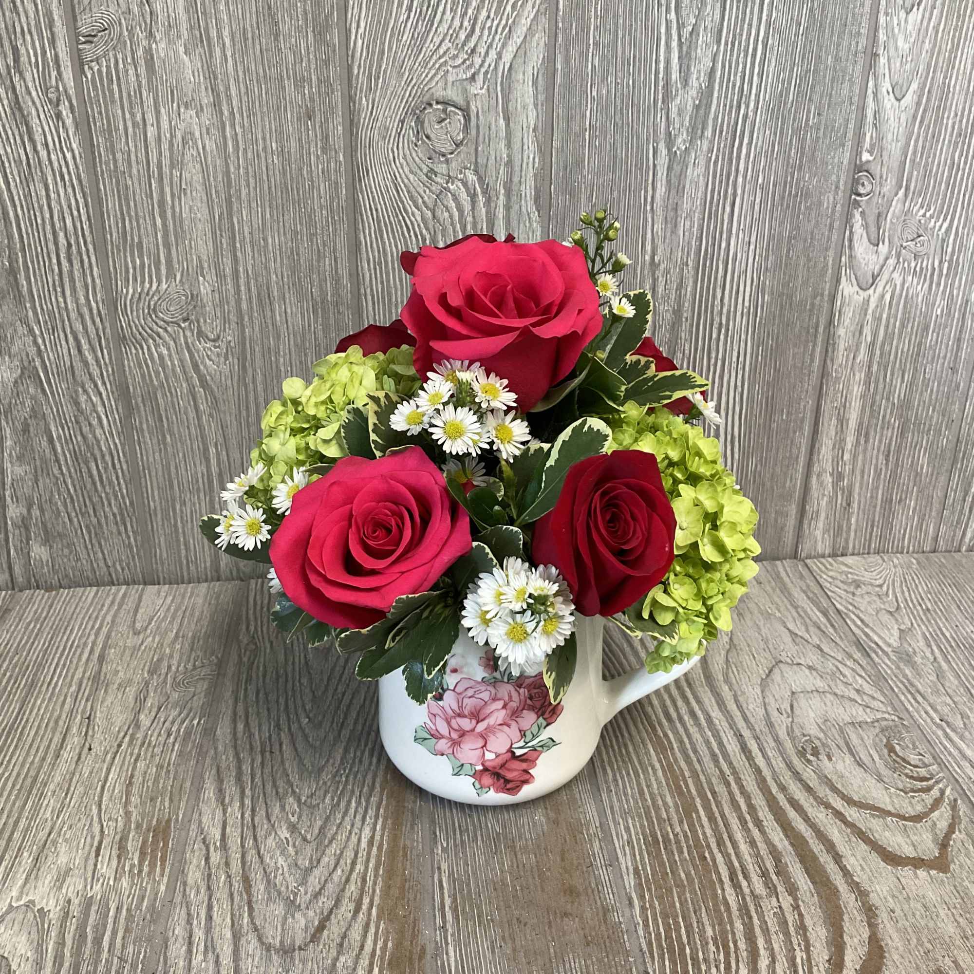 Pink and red roses with white daisies in a floral mug