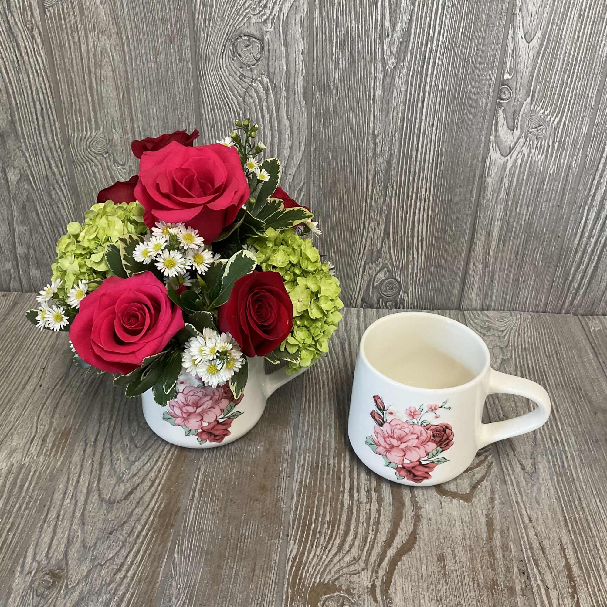 Pink and red roses arranged in a floral mug beside a matching mug.