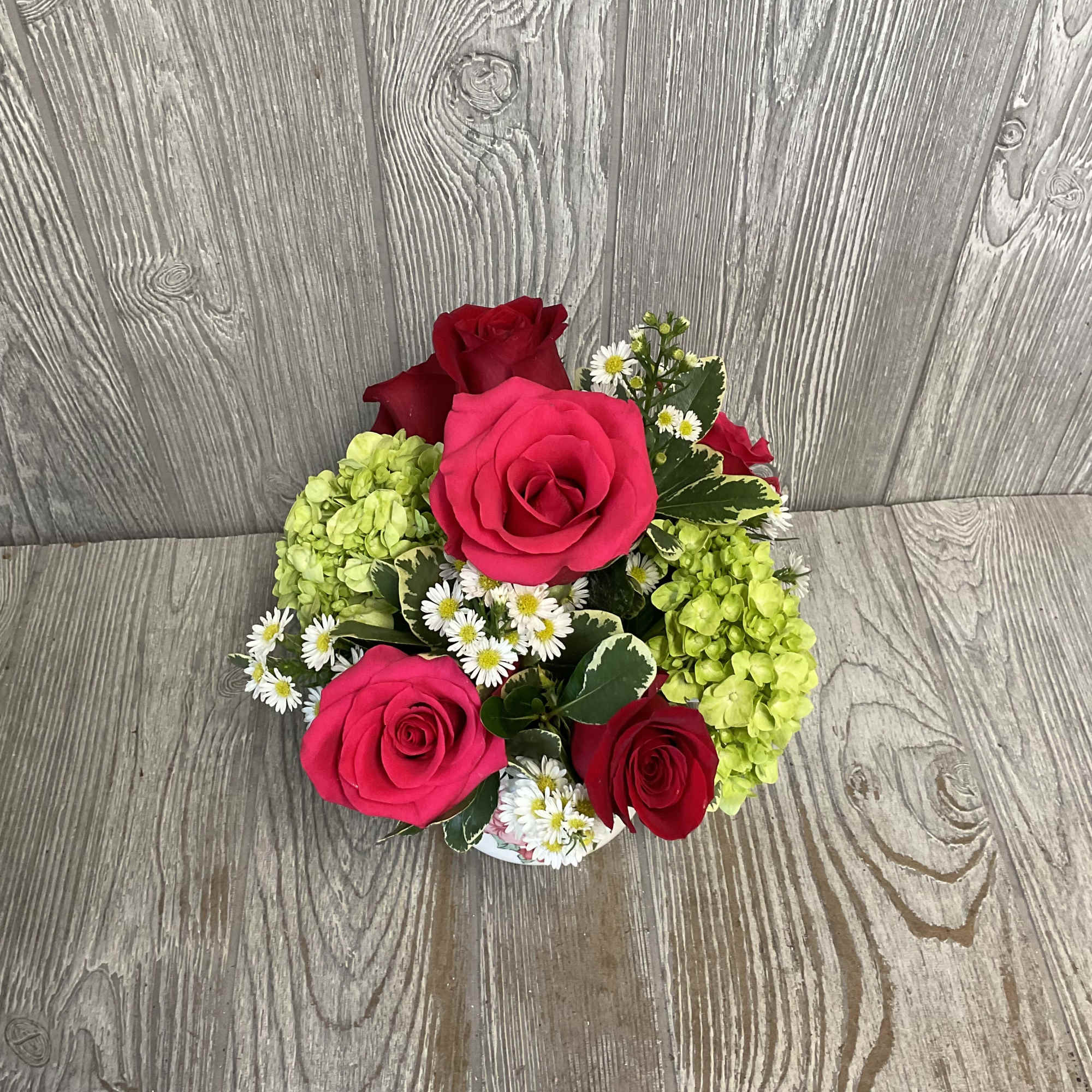 Compact bouquet of hot pink and red roses with small white daisies