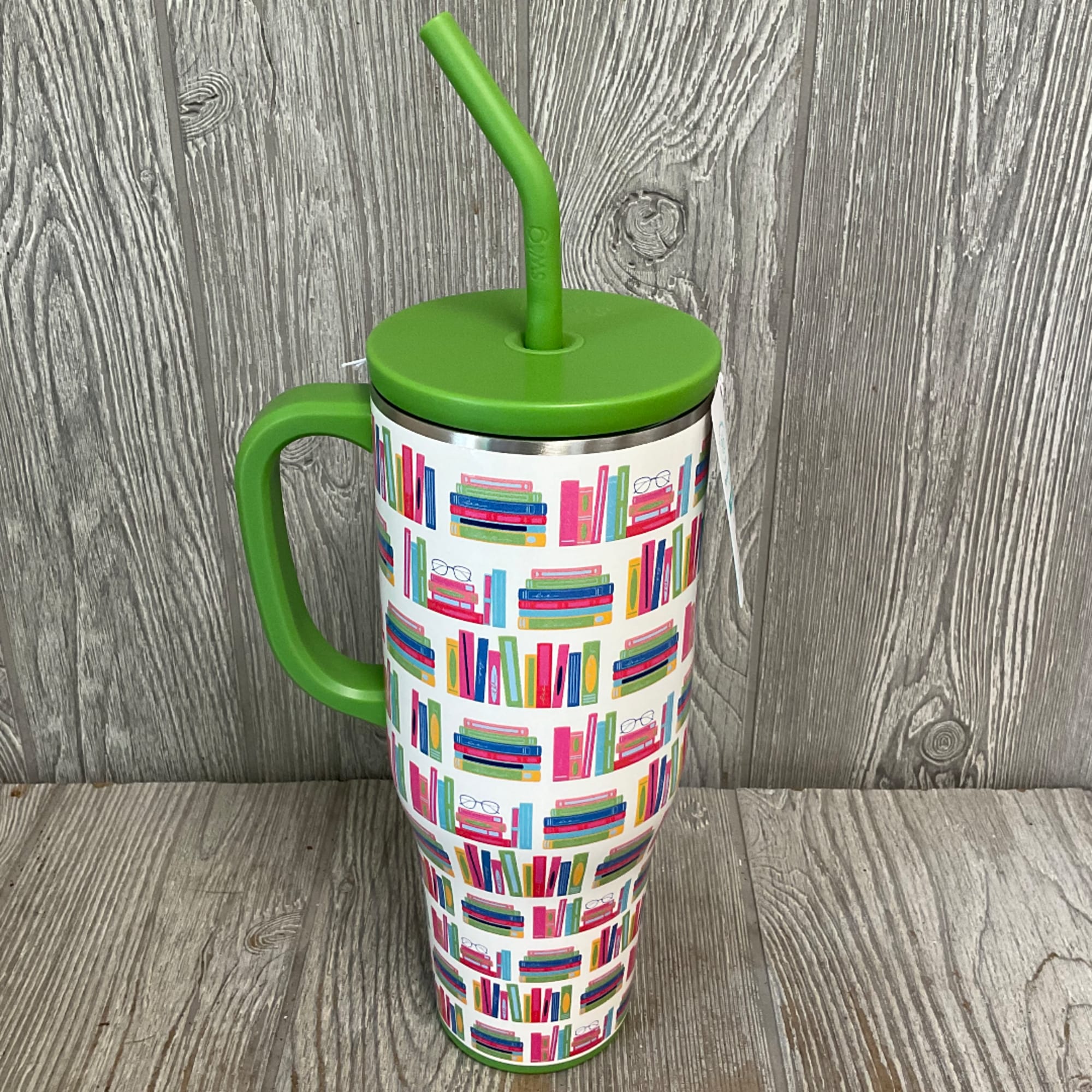 Tall insulated tumbler with a green lid, handle, and straw, covered in a colorful bookshelf pattern.