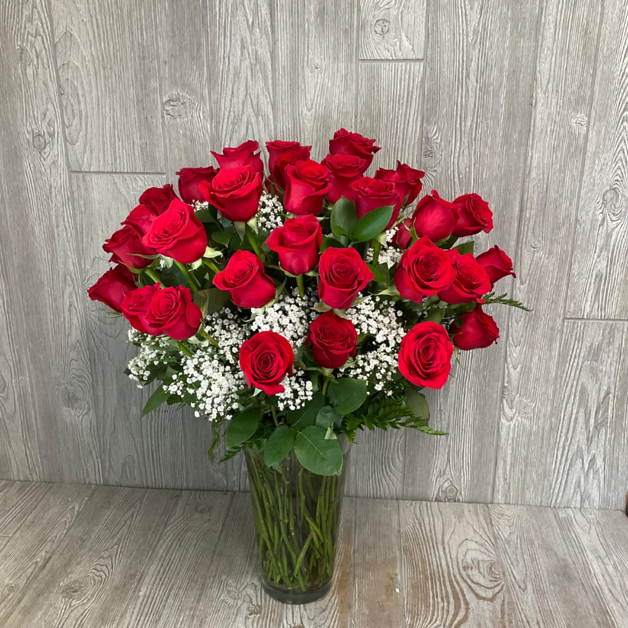 Red roses arranged in a clear glass vase with white filler flowers