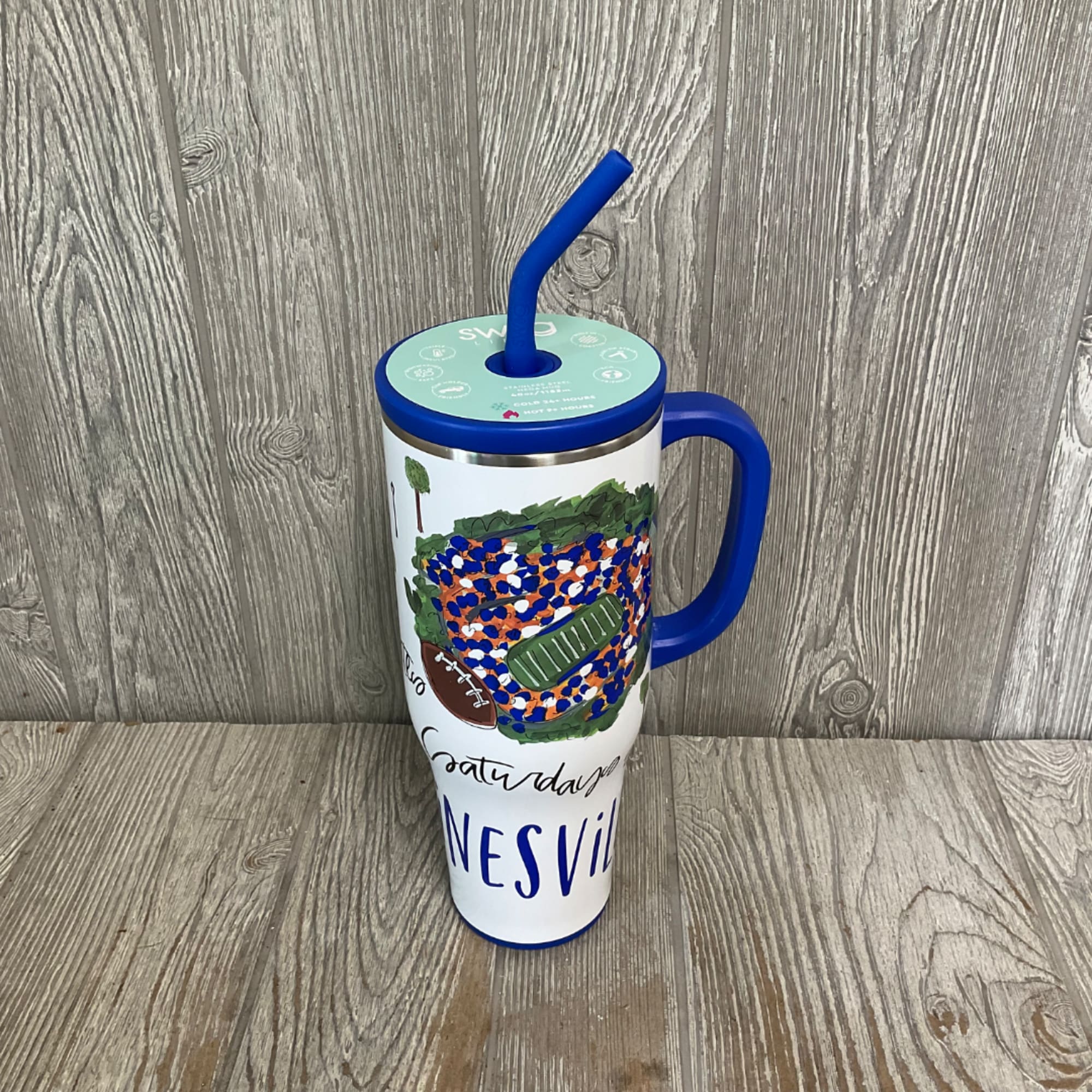 A tall insulated tumbler with a blue handle and straw, decorated with football-themed artwork.