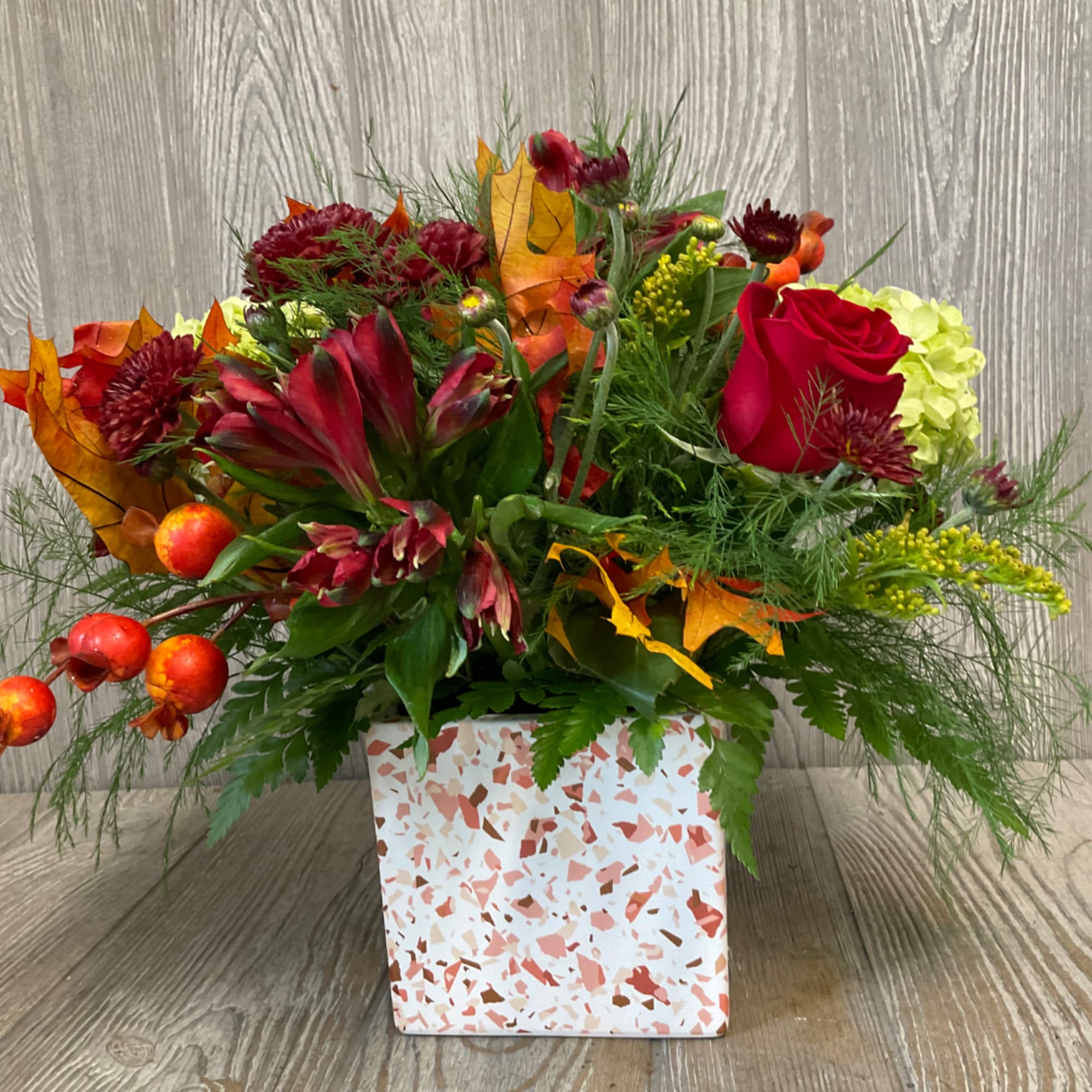 Autumn floral arrangement in a speckled square vase with red and orange blooms