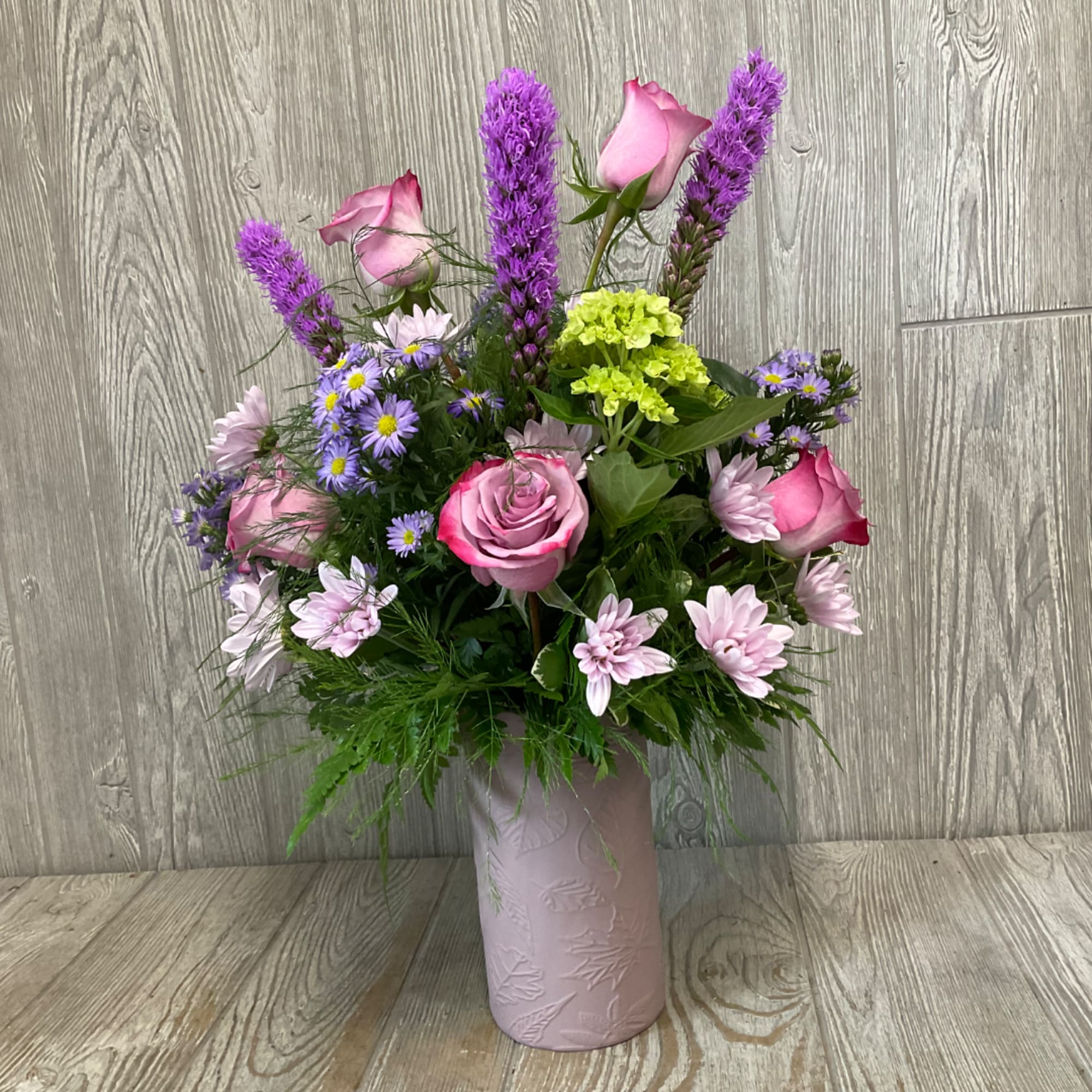 Pink roses and purple flowers arranged in a pale vase