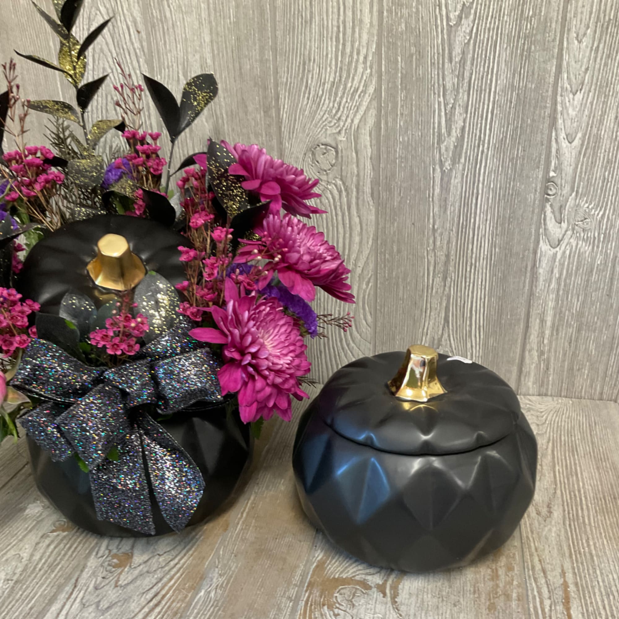 Magenta flower arrangement in a black pumpkin-shaped container with a glittery bow