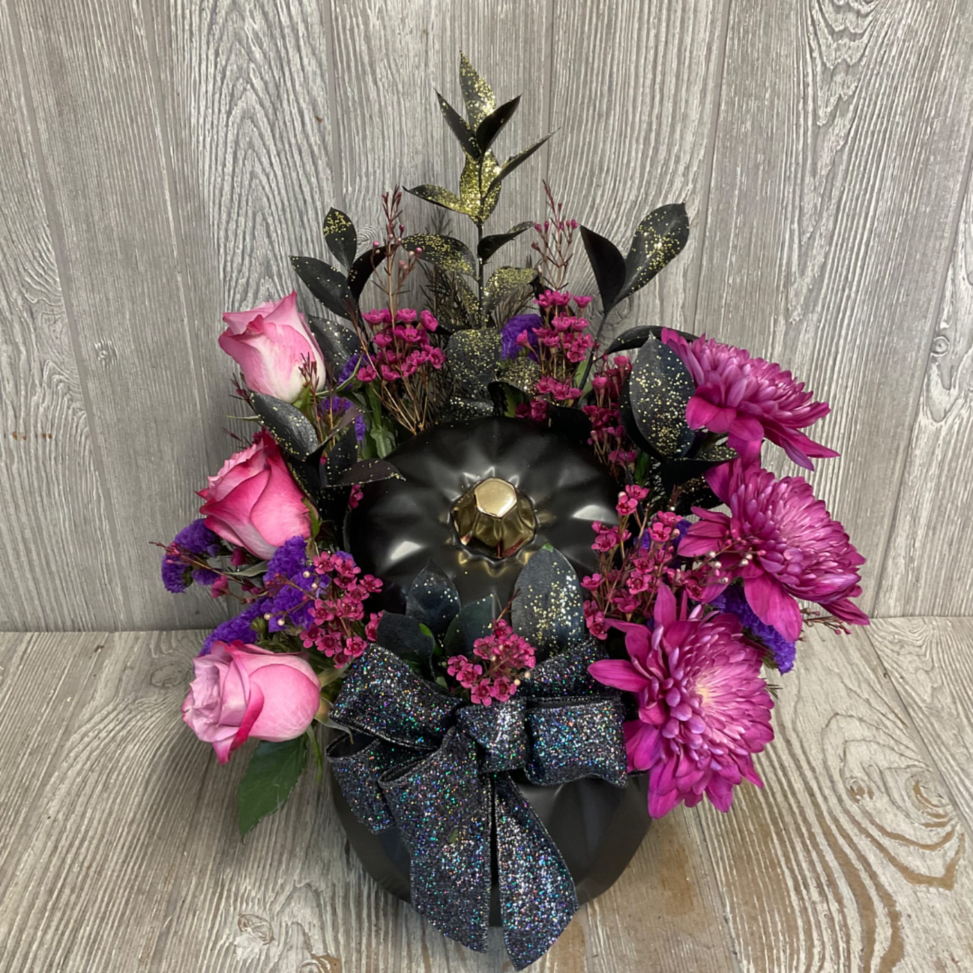 Pink roses and purple mums arranged in a black container with a glittery bow