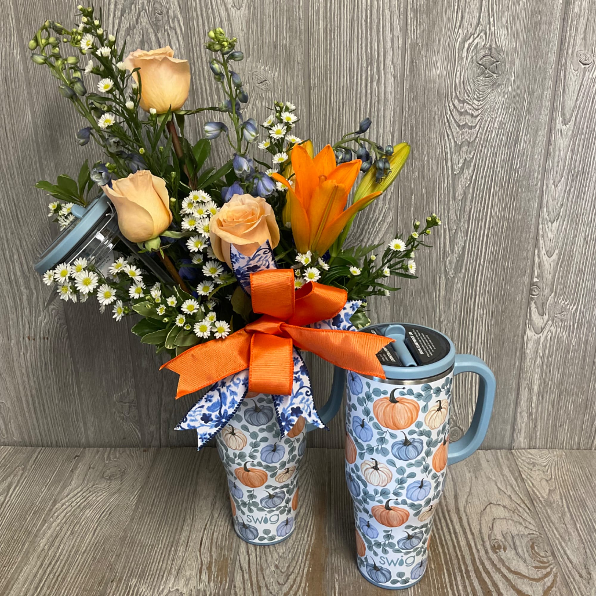 Bouquet of peach roses and orange lilies in a patterned tumbler with ribbon