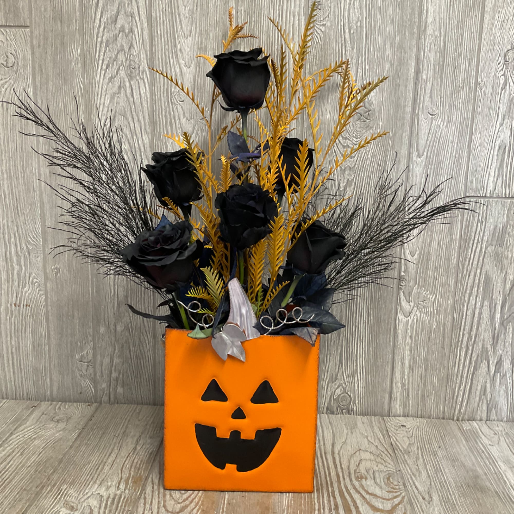 Black roses in an orange jack-o'-lantern container with tall black accents