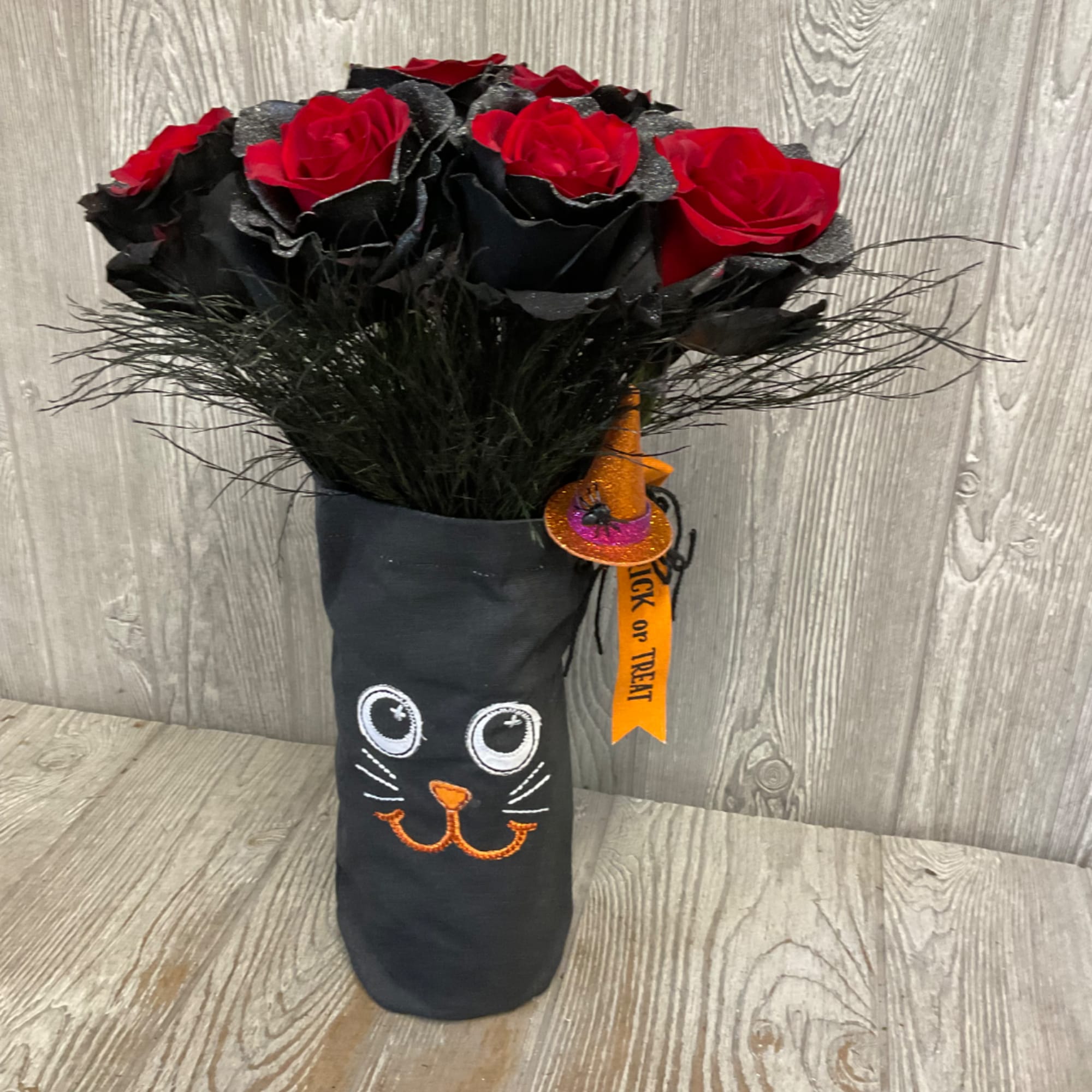 Red roses in a black Halloween-themed vase with a cat face and witch hat tag