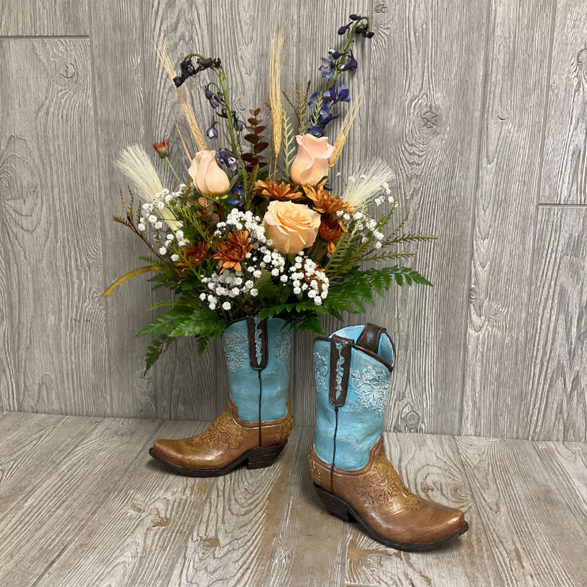 Floral arrangement in cowboy boots with peach roses and blue flowers