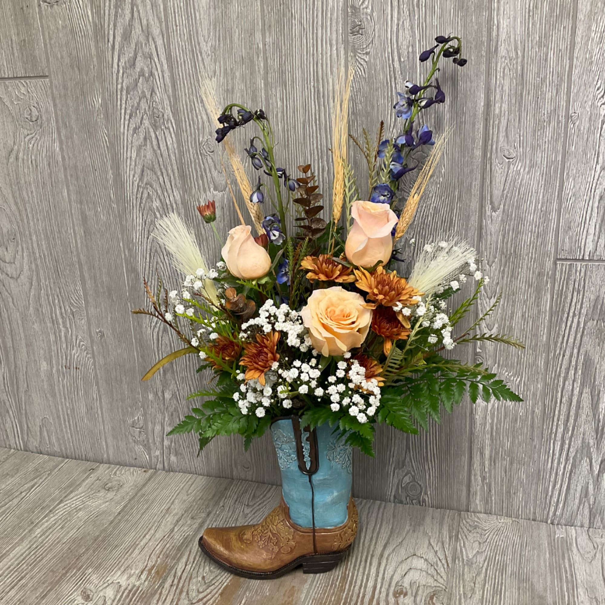 Floral arrangement in a blue cowboy boot vase with peach roses and blue flowers