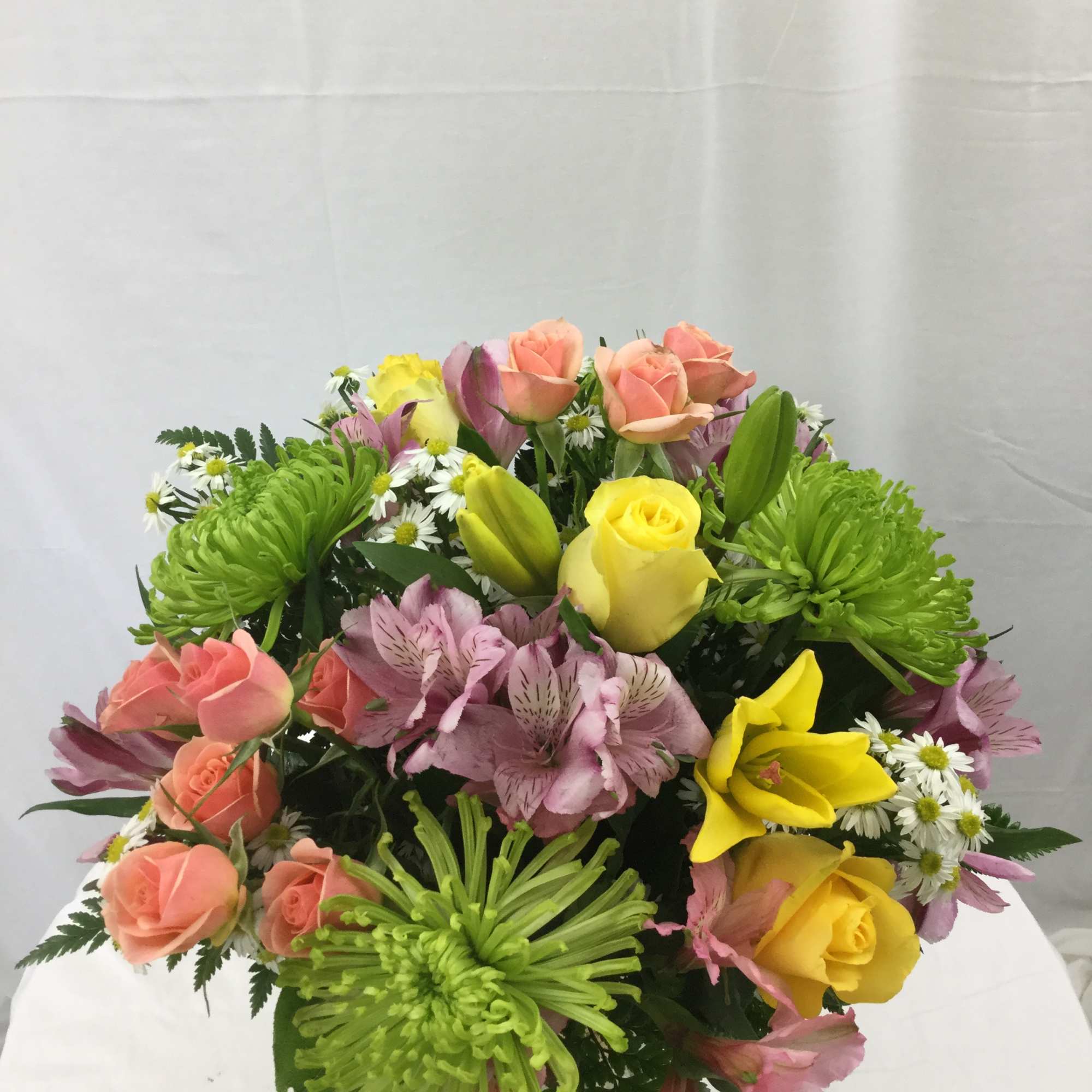 Mixed bouquet with peach roses, yellow lilies and roses, green mums, and pink alstroemeria in a glass vase