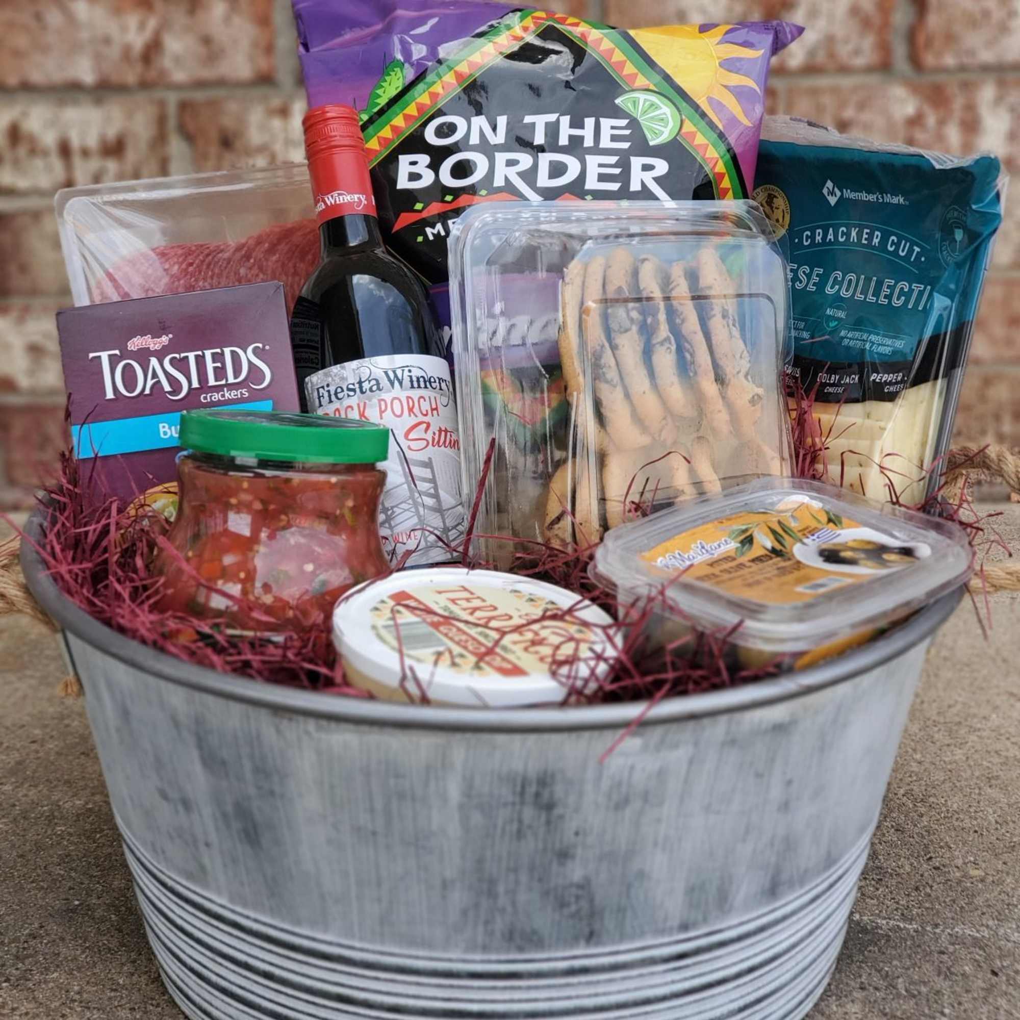 Gift basket with wine, crackers, chips, dip, and snacks in a metal tub