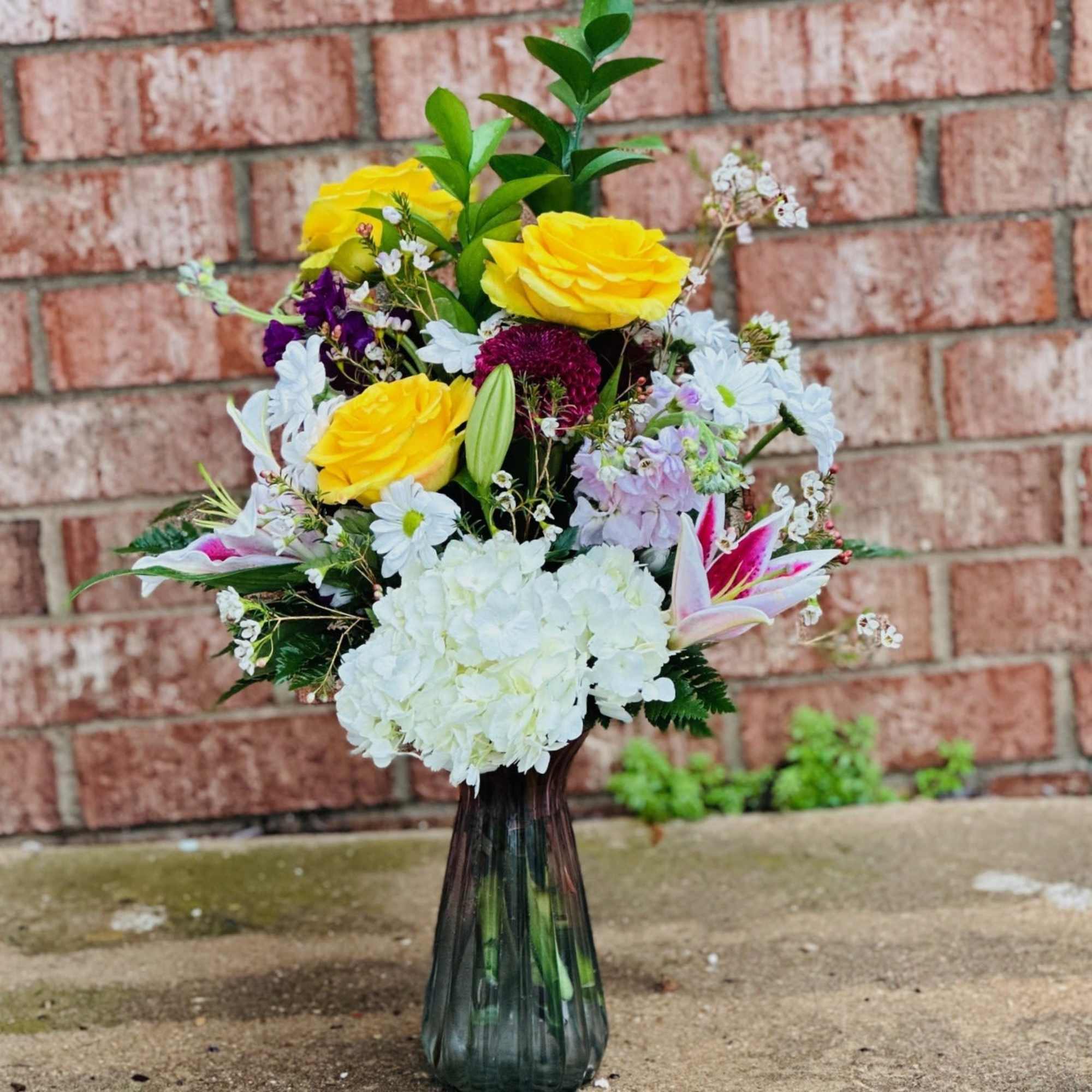 Mixed bouquet of yellow roses, white hydrangea, and lilies in a glass vase