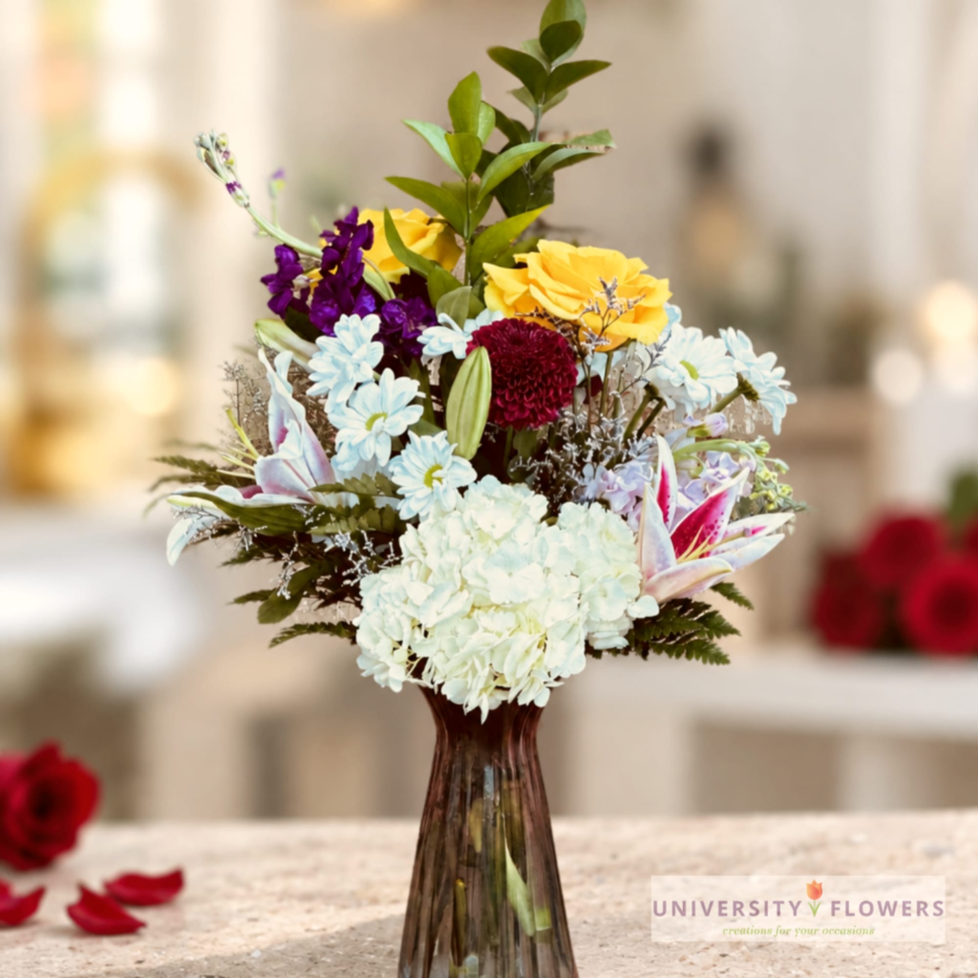 Mixed bouquet in a tall glass vase with yellow, blue, purple, and white flowers