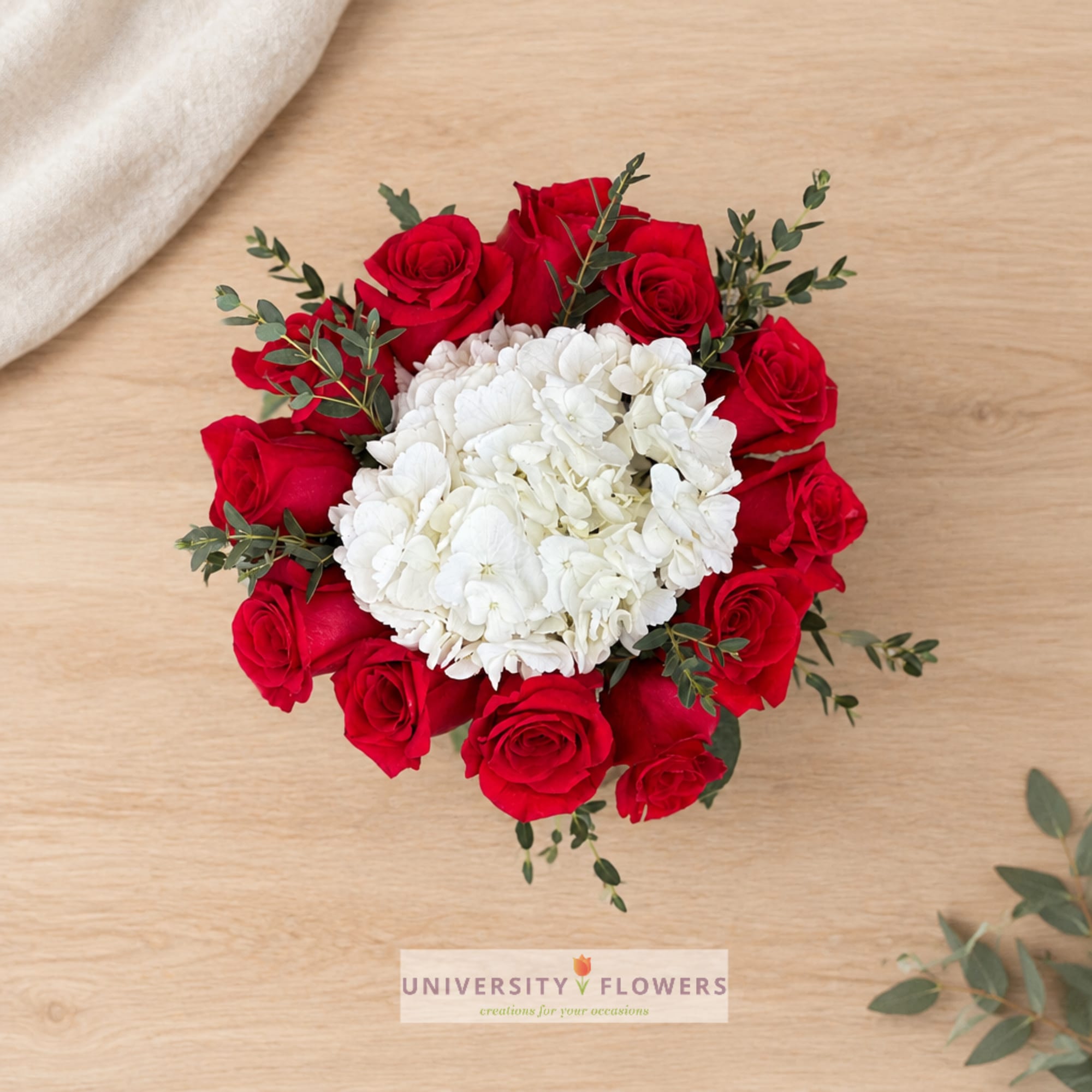 Red roses surrounding a white hydrangea cluster on a wooden surface