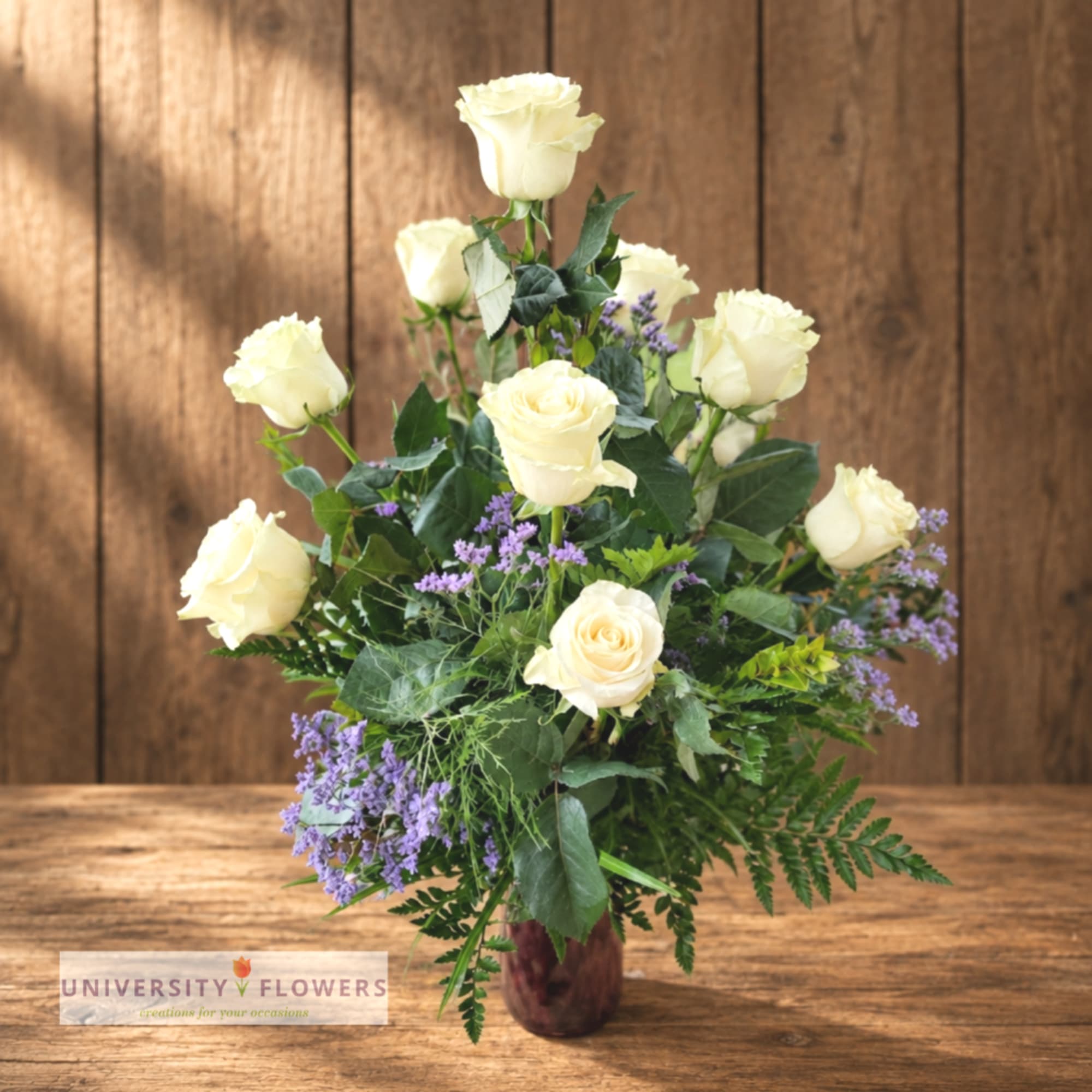 Cream roses arranged in a burgundy vase with purple filler flowers