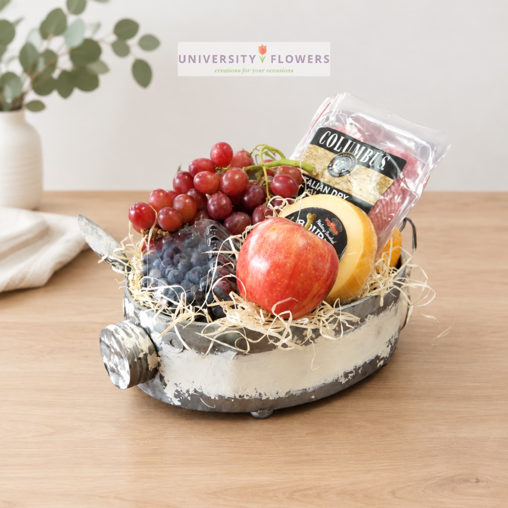 Fruit gift basket with grapes, an apple, and packaged cheese in a metal container
