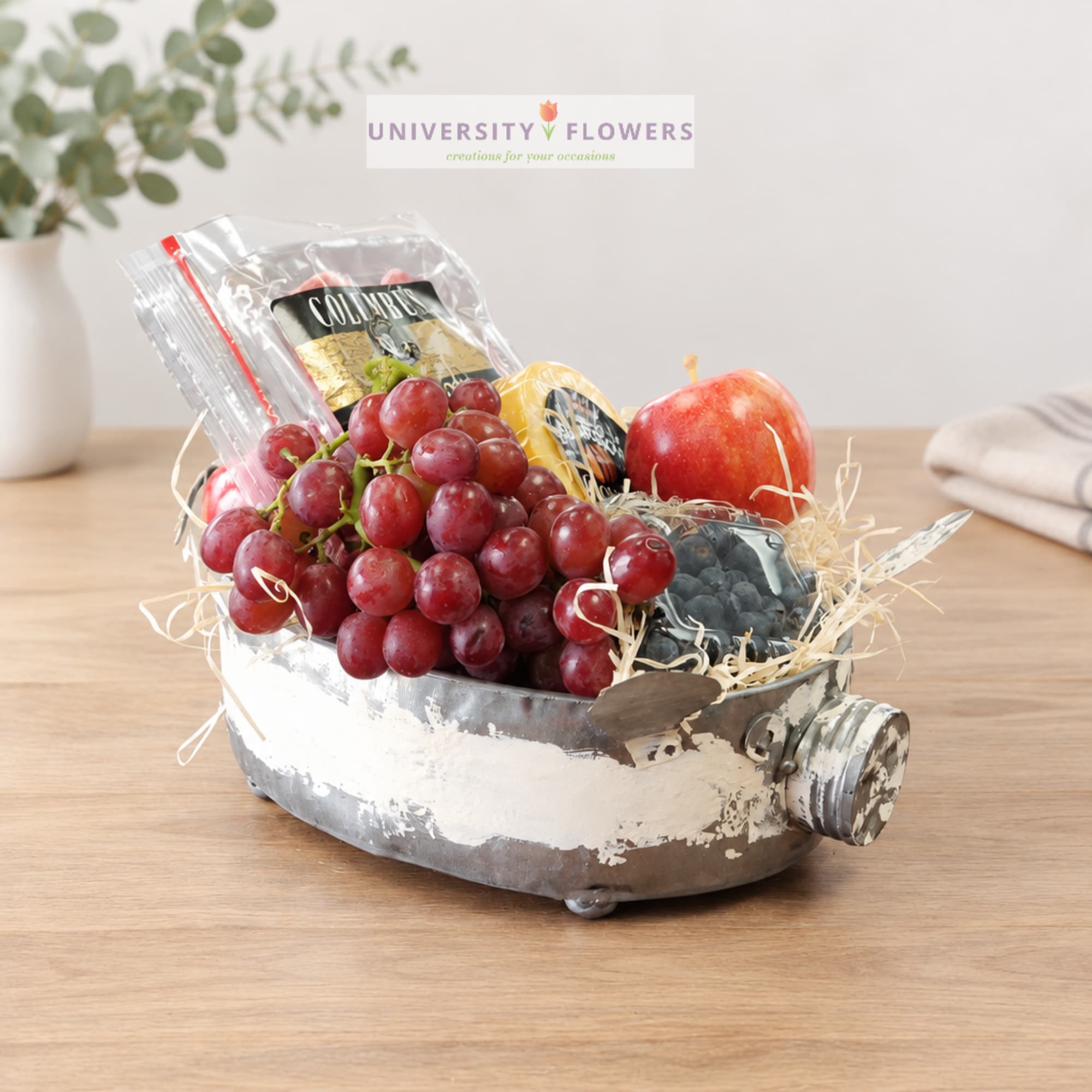 Fruit gift basket in a metal container with grapes, apples, and packaged snacks