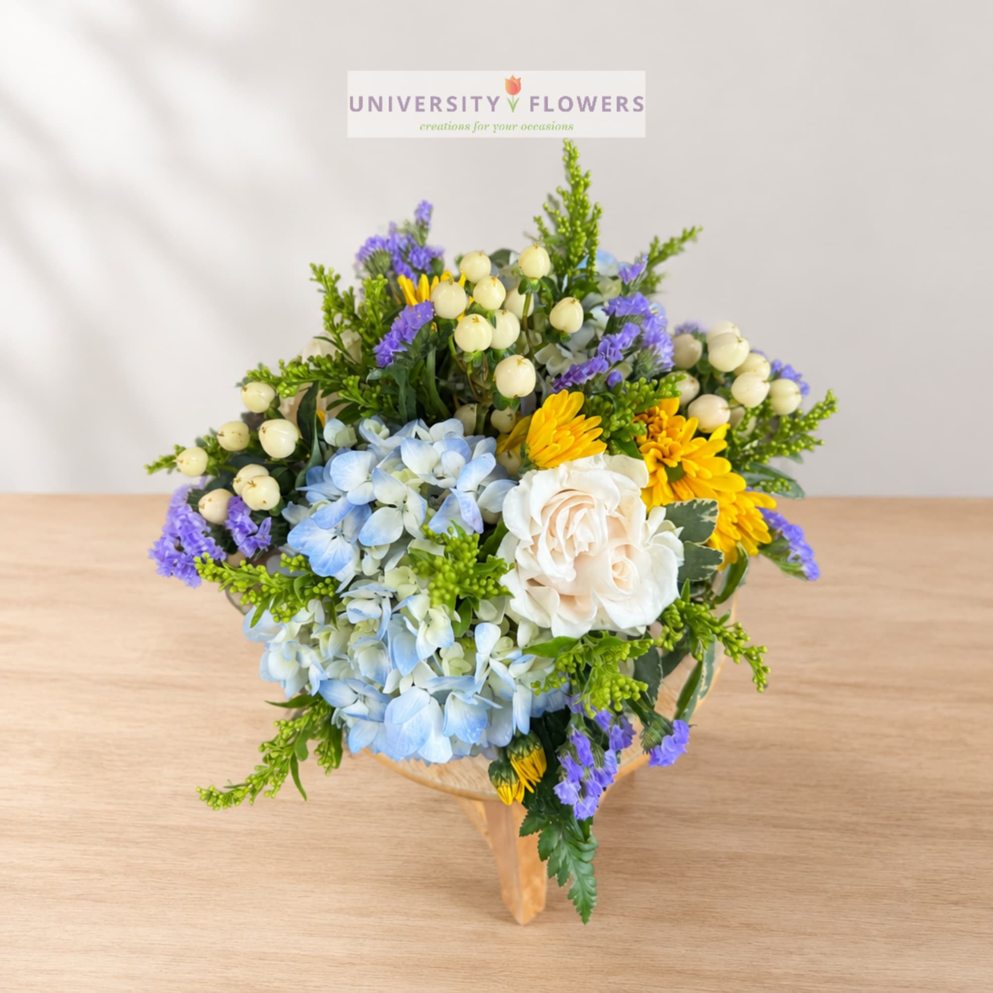 Mixed bouquet with blue hydrangeas, white roses, and yellow daisies in a wooden holder