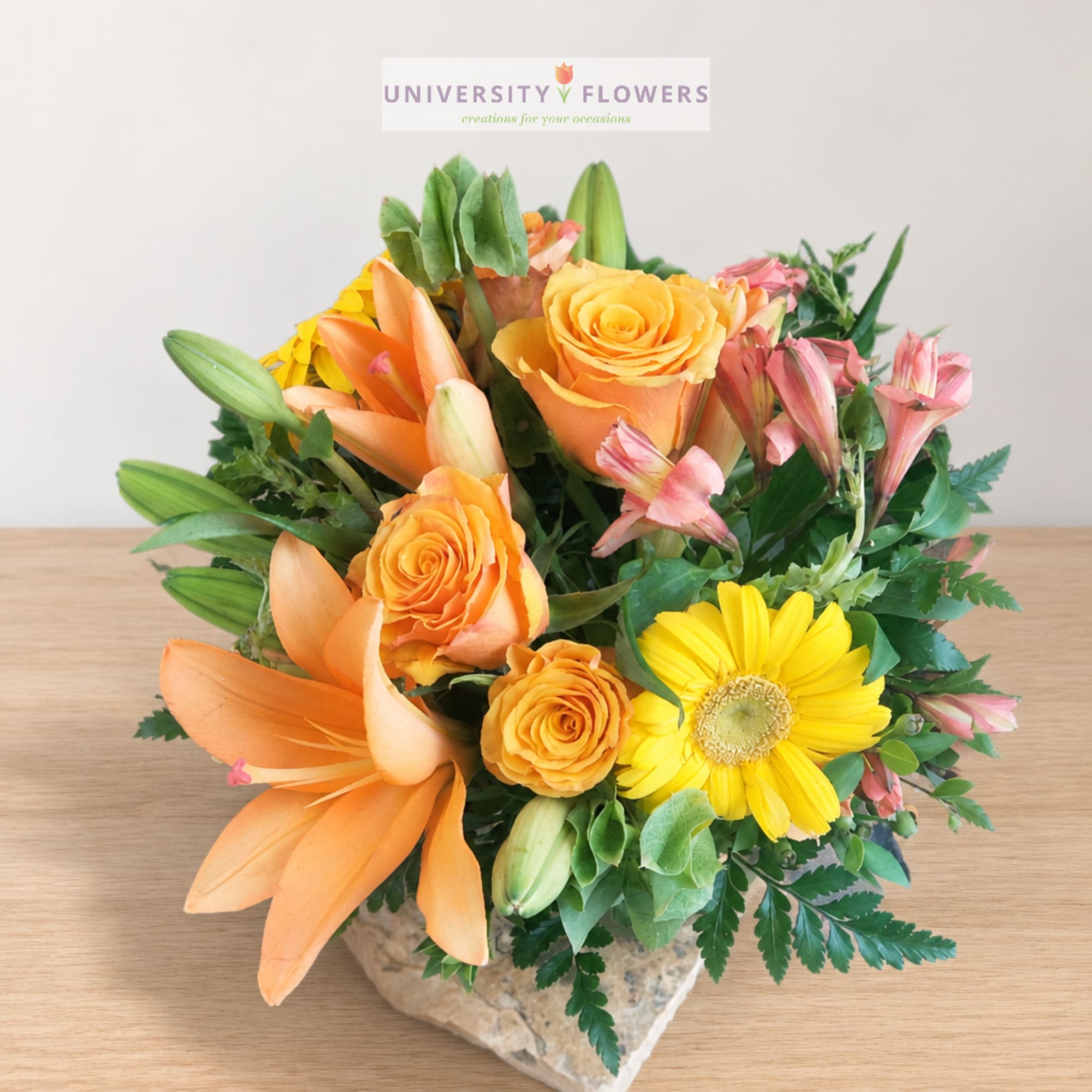 Orange roses, lilies, and yellow gerbera daisy in a stone vase