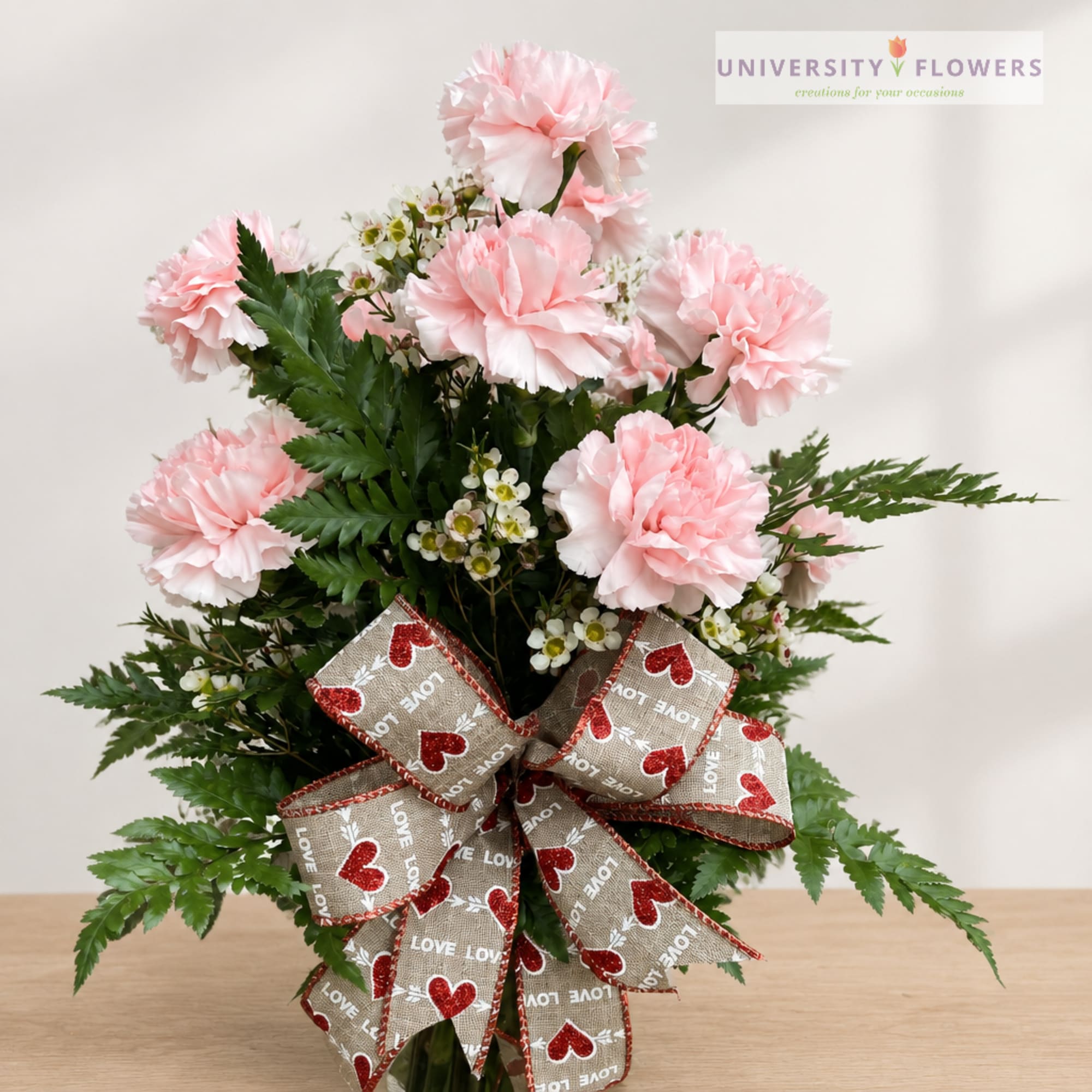 Pink carnations with small white filler flowers and a heart-patterned bow
