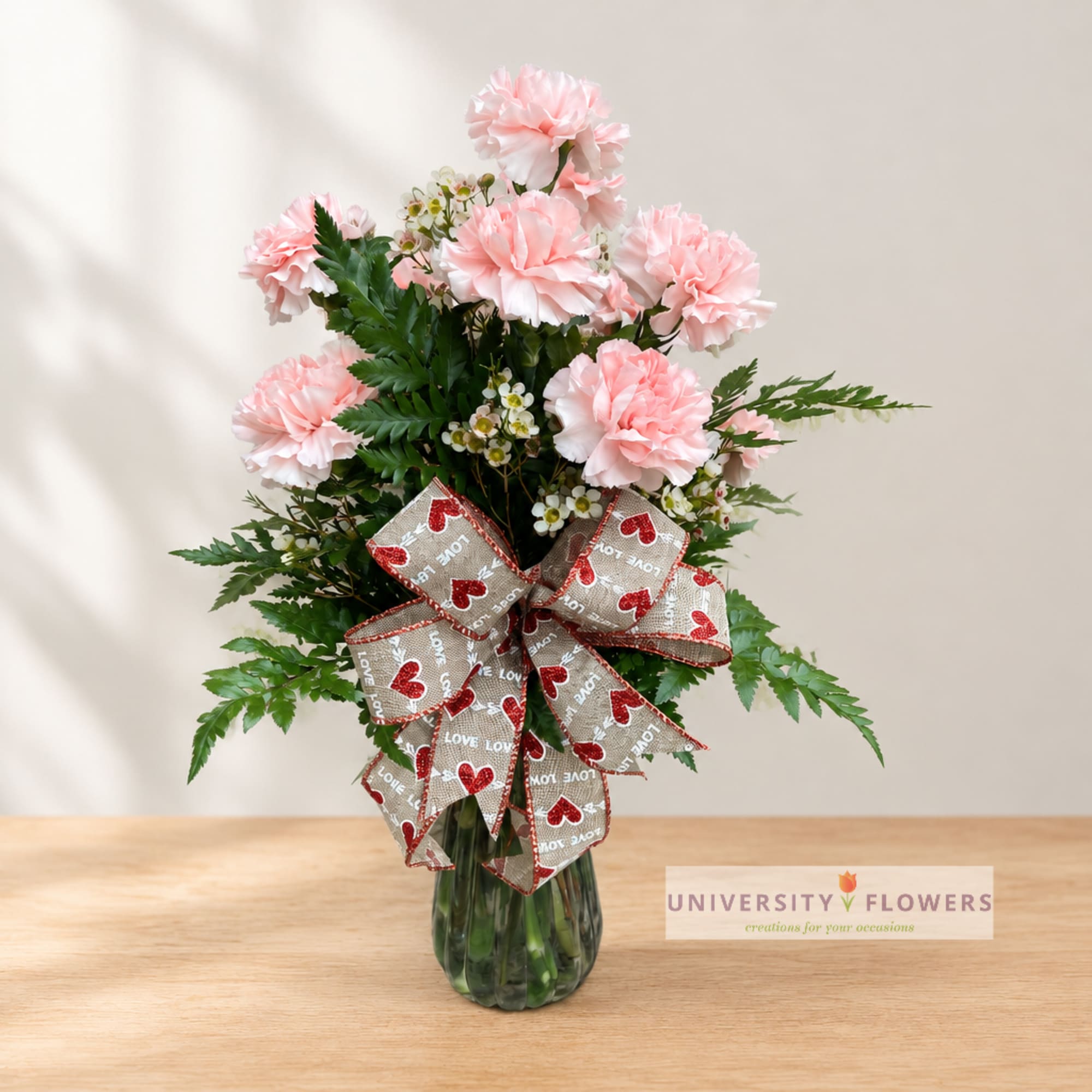Pink carnations in a glass vase with a heart-patterned bow
