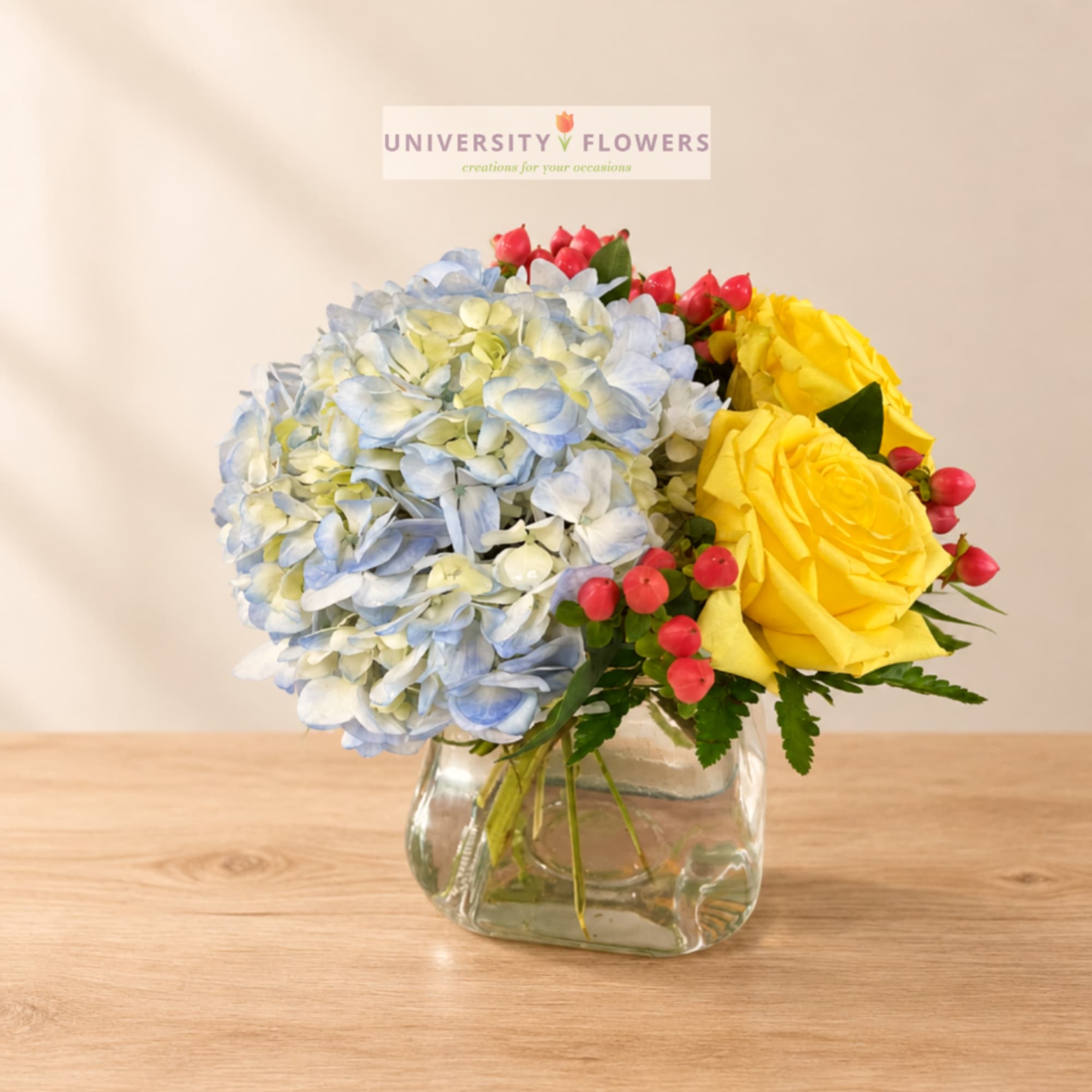 Blue hydrangeas and yellow roses in a clear glass vase