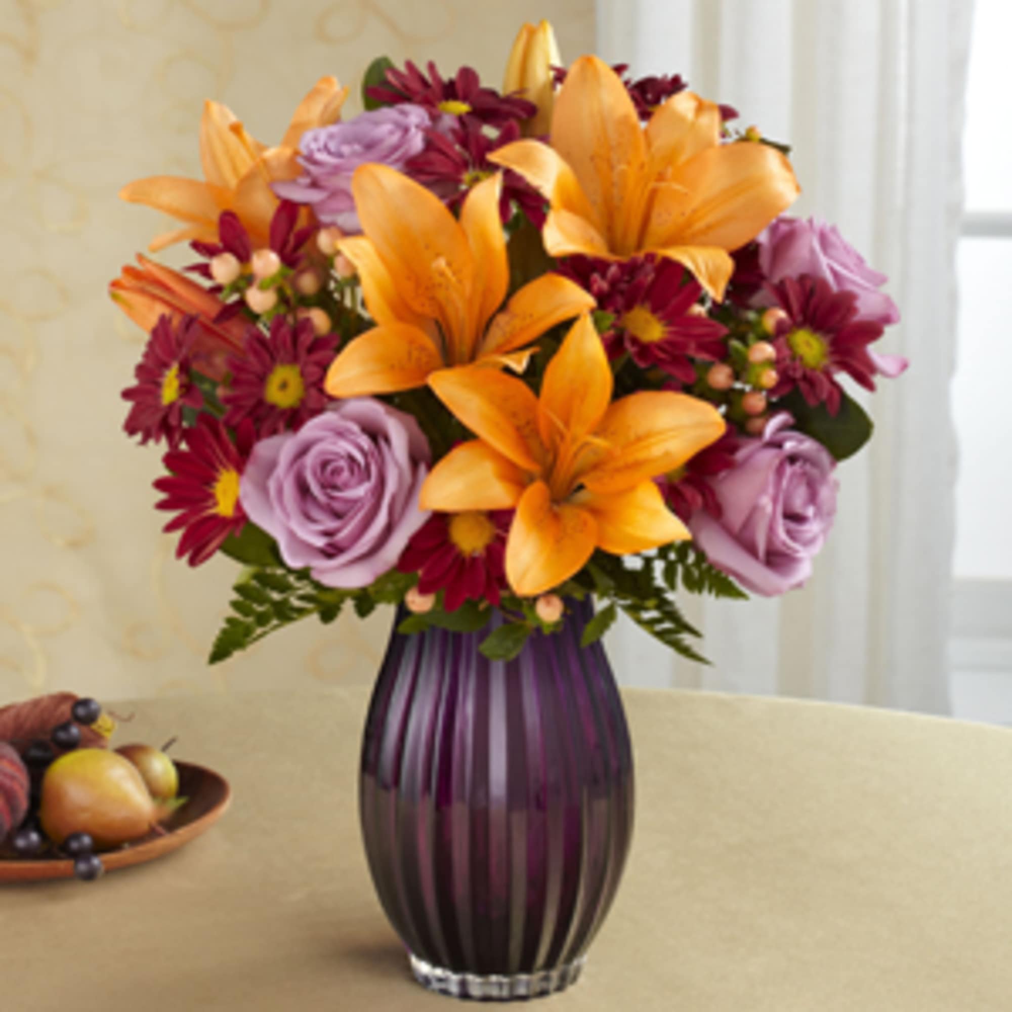 Orange lilies and purple flowers in a tall purple vase