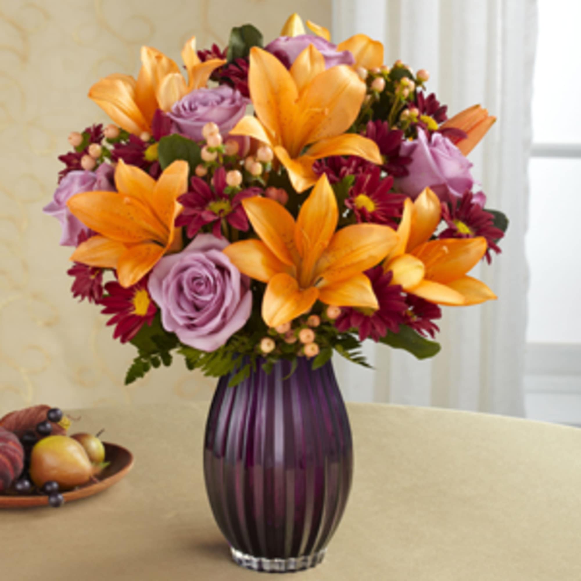 Orange lilies and purple roses in a purple glass vase