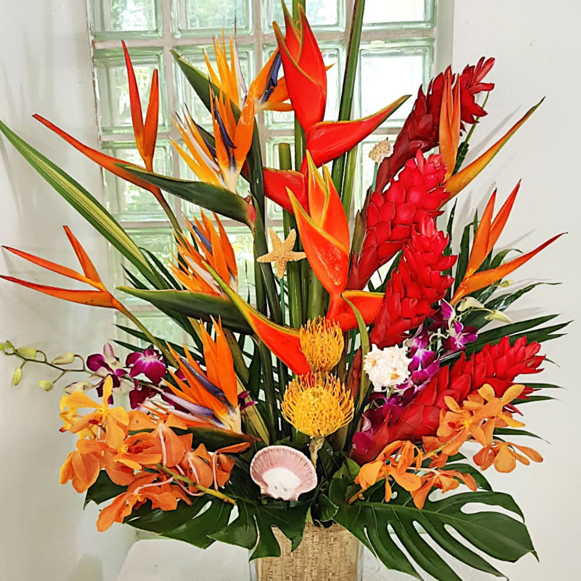 Tropical arrangement with orange bird-of-paradise and red ginger flowers in a woven vase